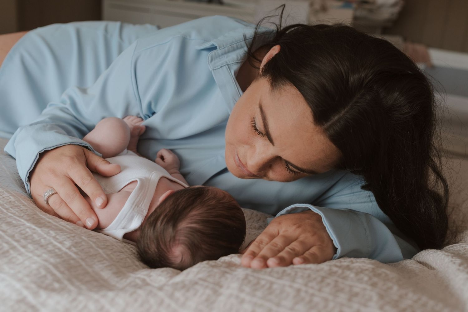 Baby sleeping peacefully on white bedding with hand reaching to comfort them gently.