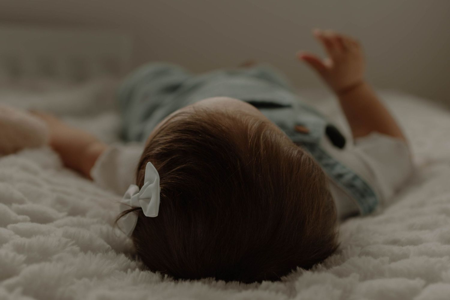 Newborn baby wrapped in soft blankets lying on white textured bedding in natural light.