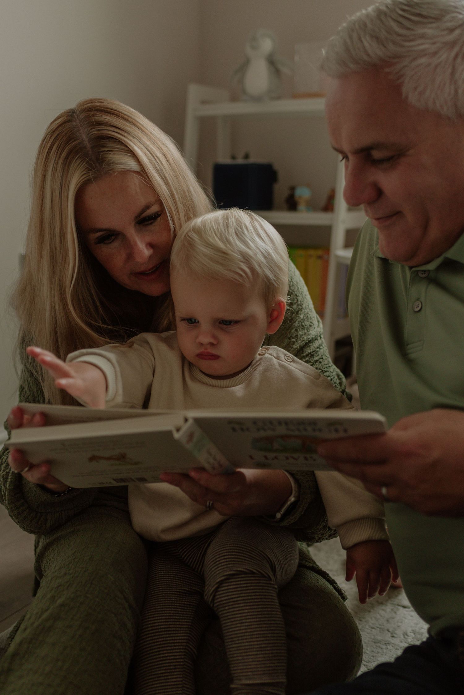 Family members sit close together reading a book in a cozy living room setting.