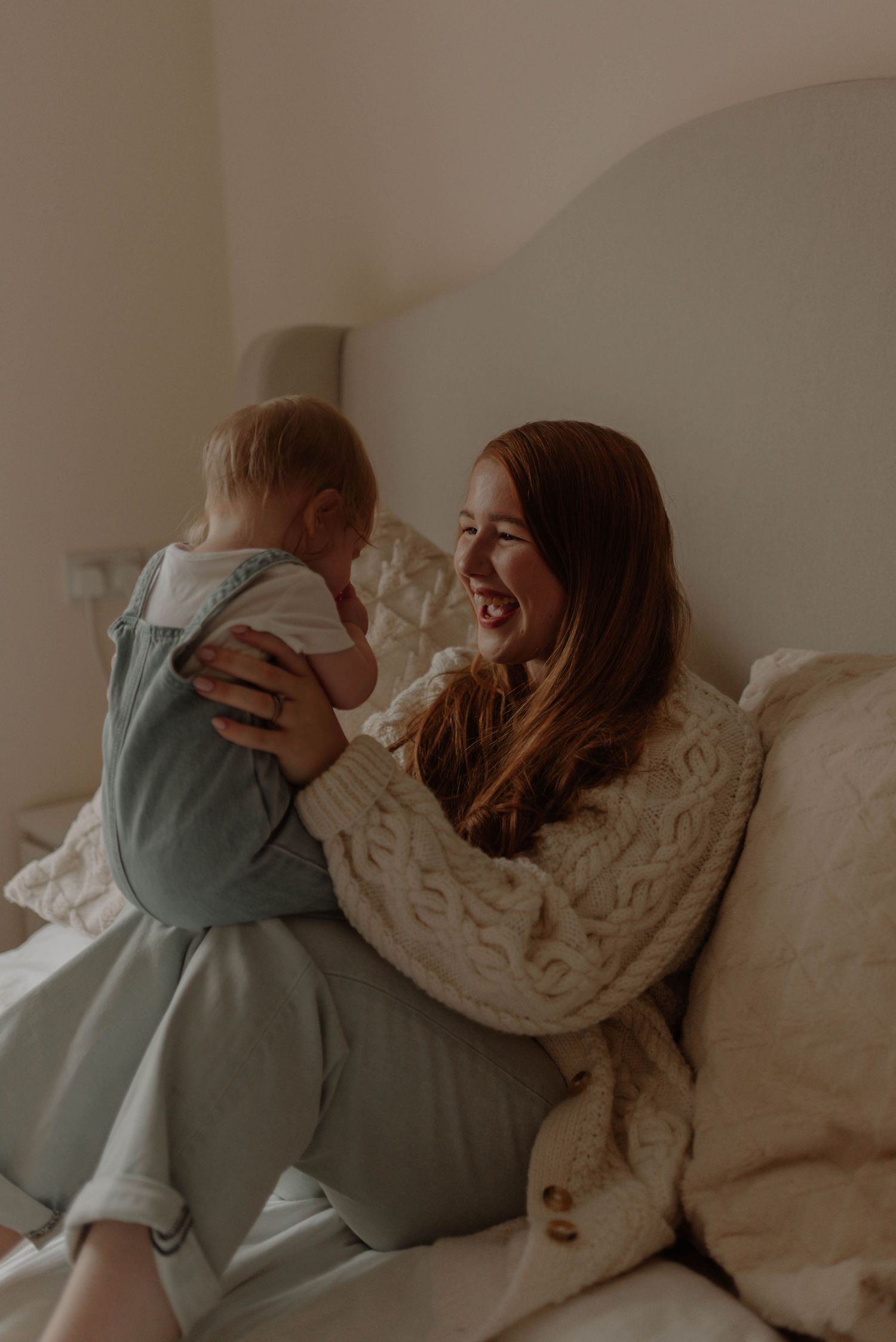 A tender moment of joy and laughter shared between a parent and baby on a cozy bed with white bedding.