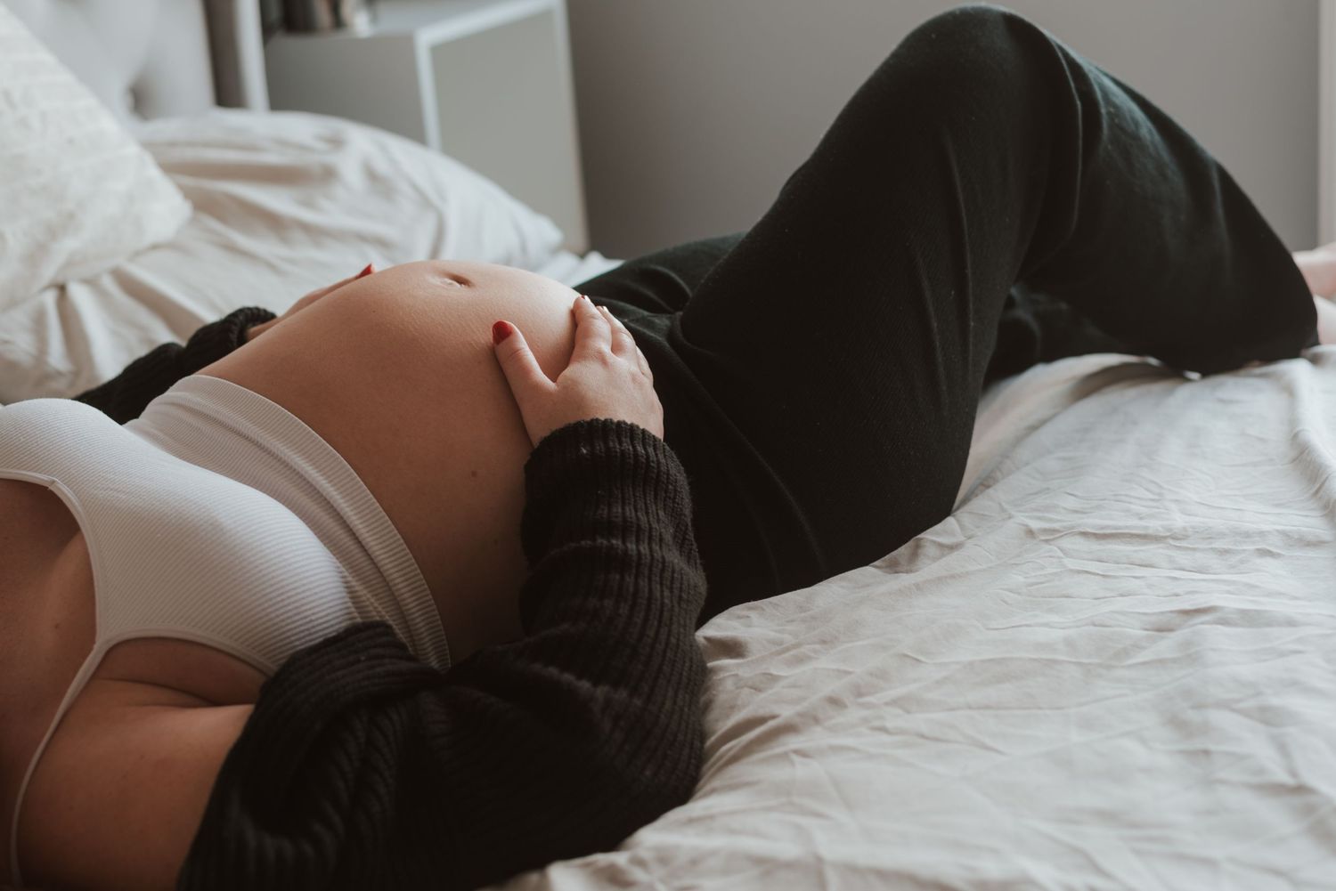 An intimate indoor maternity photo showing a pregnant belly against white bedding.