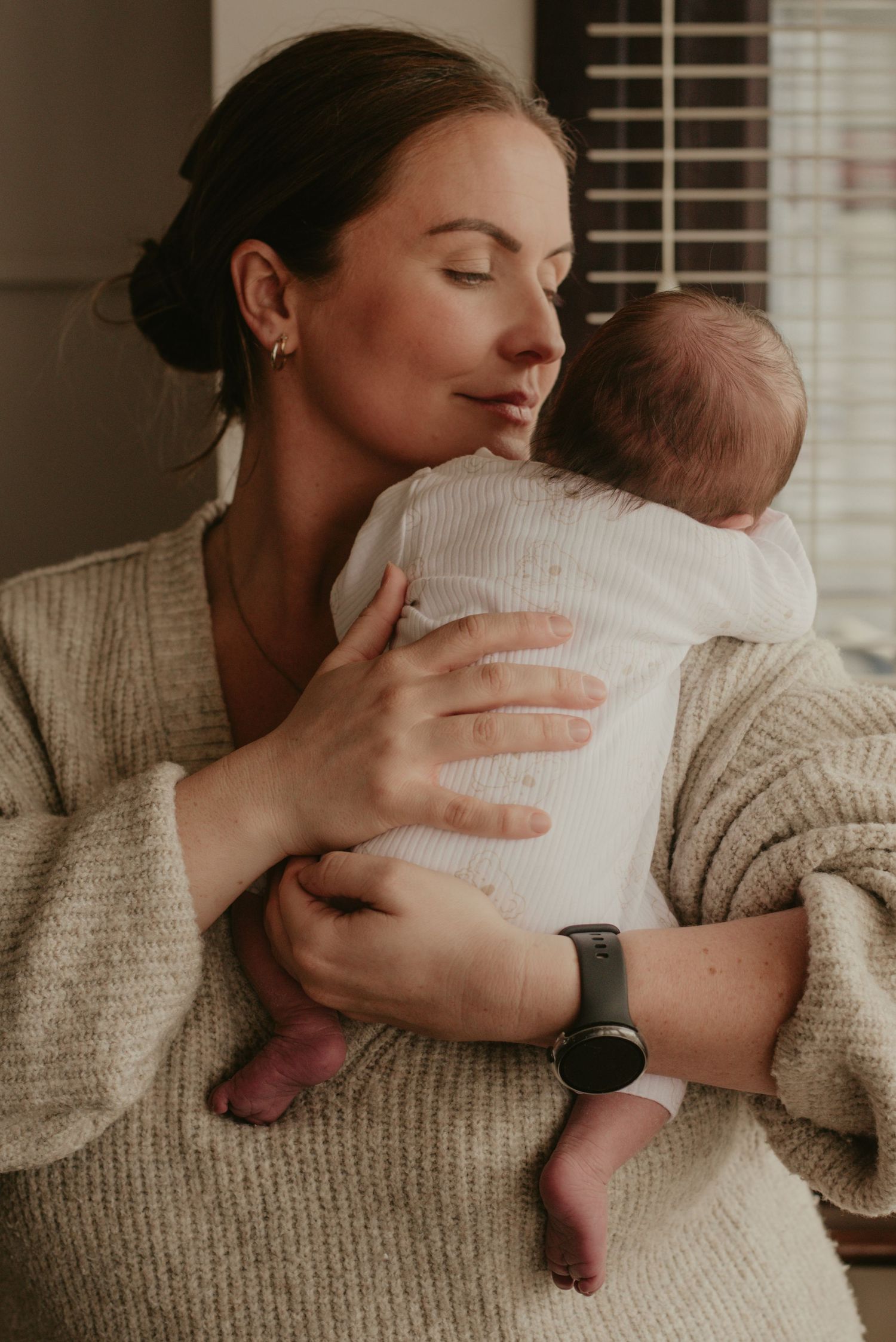 Intimate nurturing moment with baby in white clothing against neutral background.