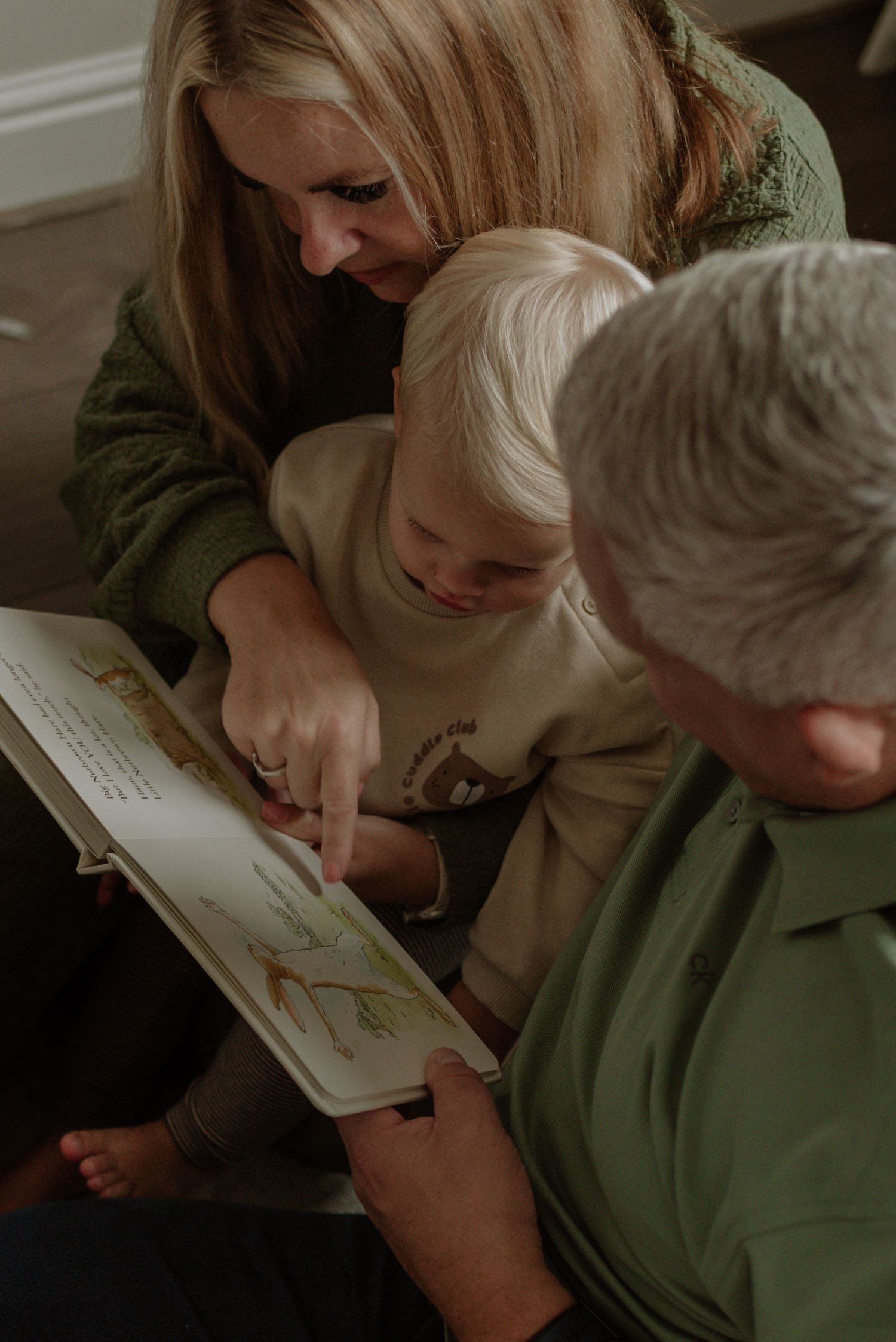 Parent and child share an intimate moment reading a picture book together in warm indoor lighting.