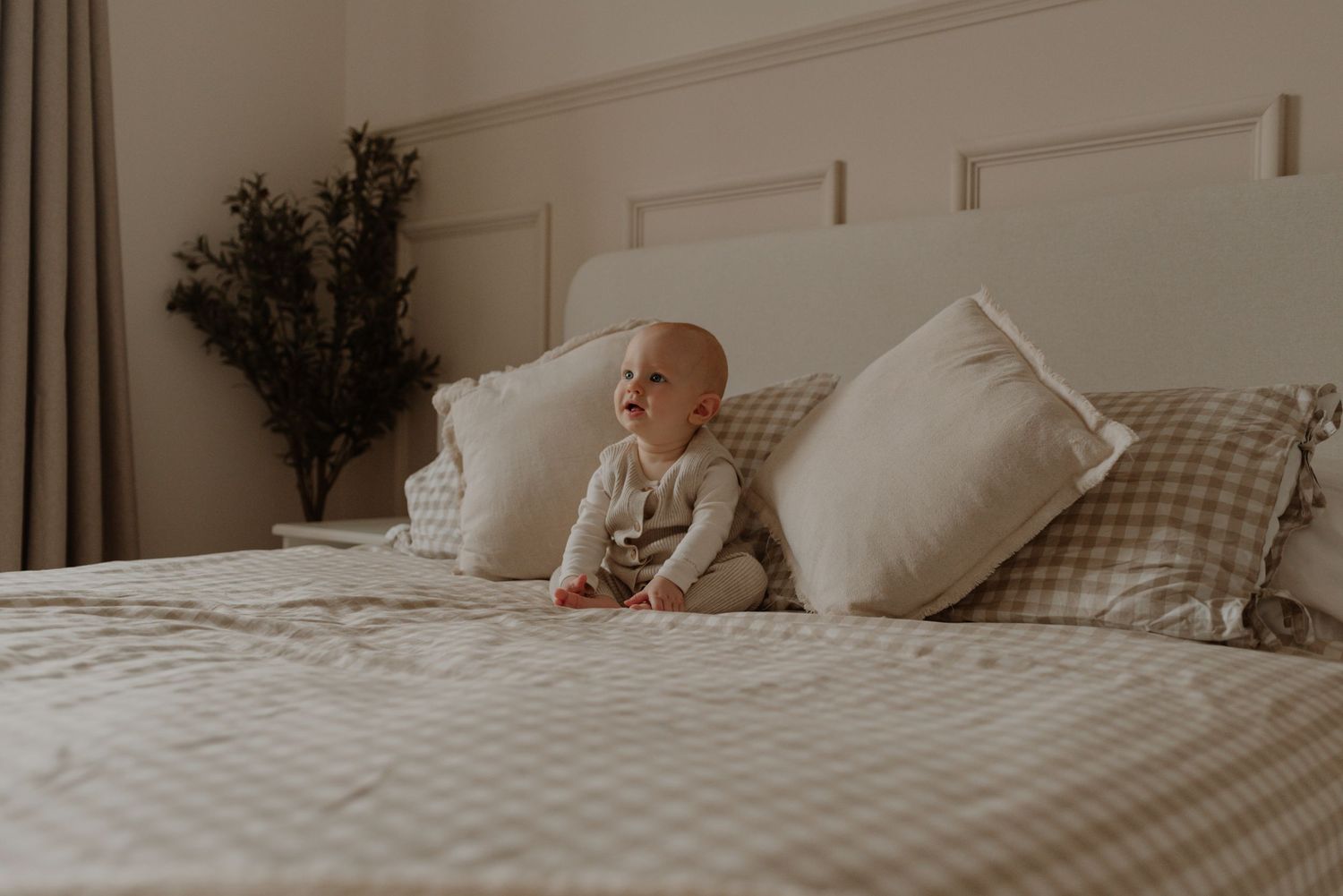Cozy neutral bedroom with white bedding, plaid pillows, and dried floral arrangements on a comfortable bed.