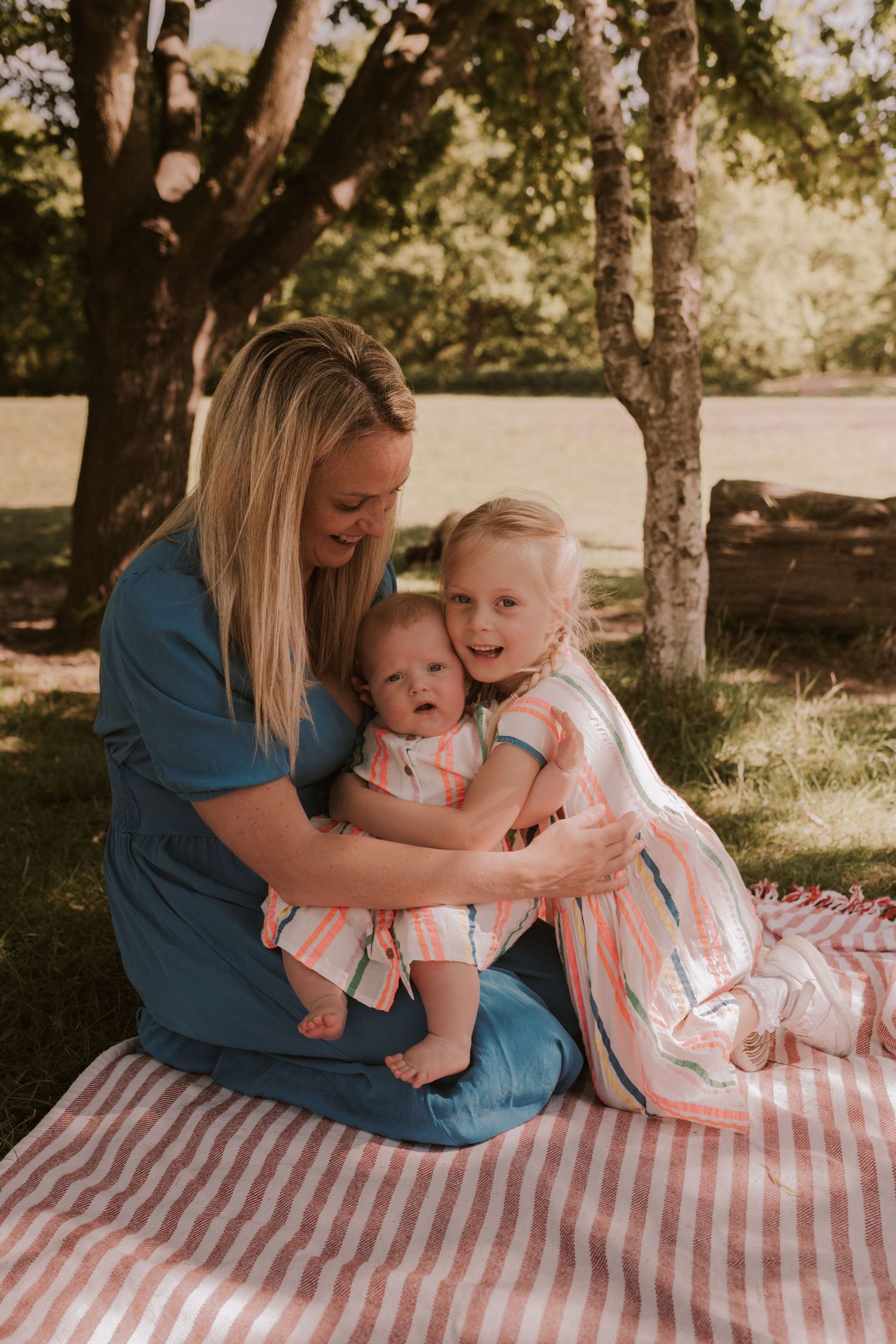 A heartwarming family embrace on a striped picnic blanket under leafy trees.