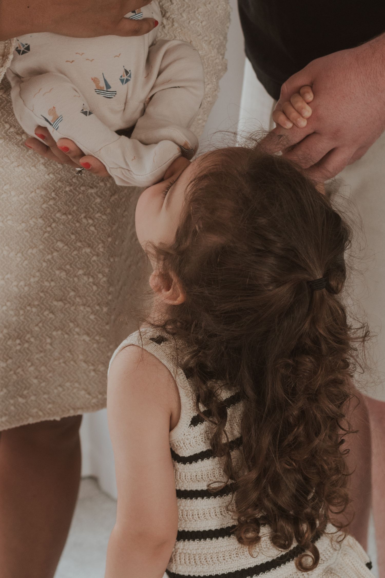 A child with curly hair reaches up to baby feet while wearing a knitted top.