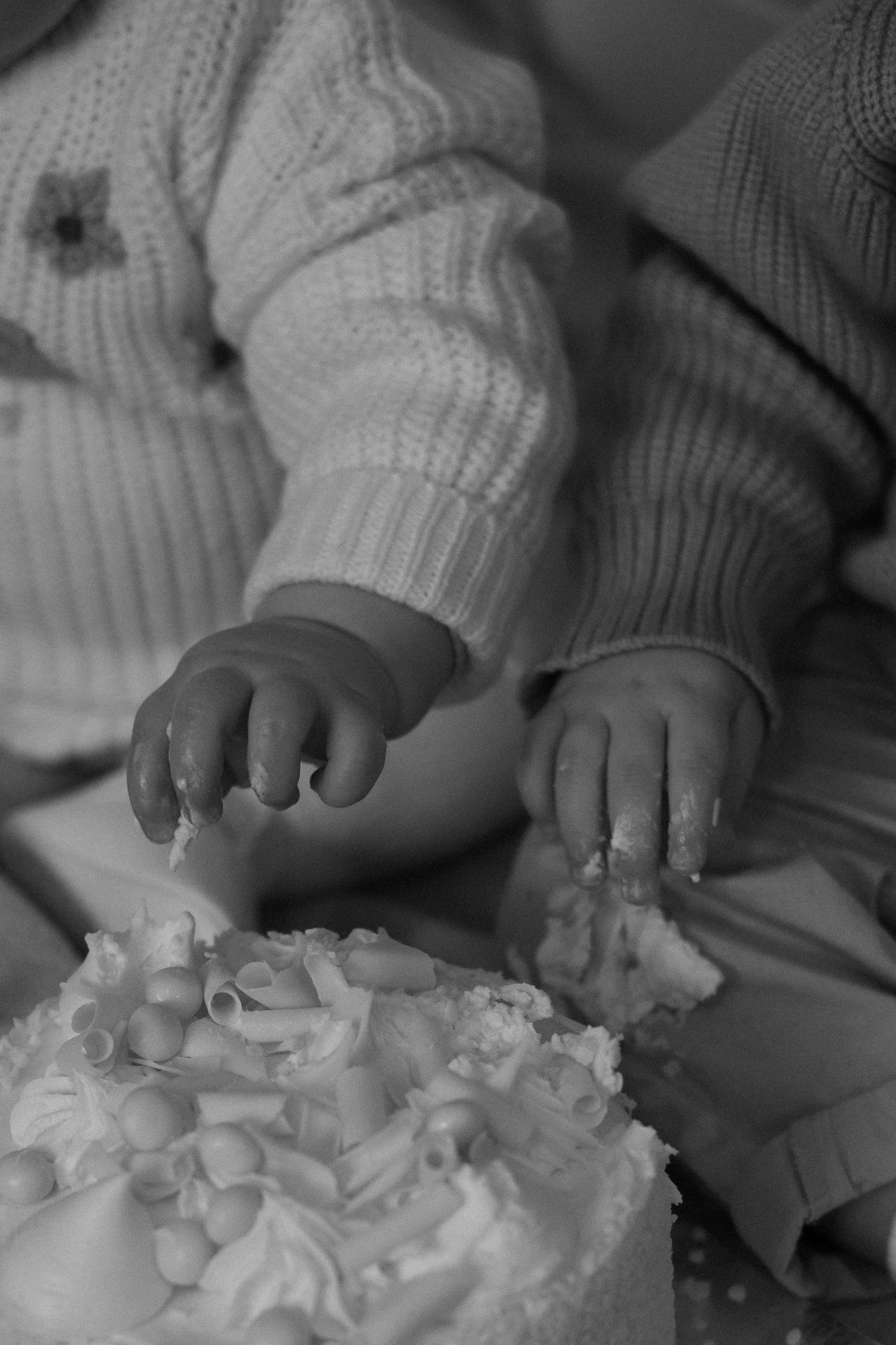 Small hands reaching to touch white frosted cake in monochrome.