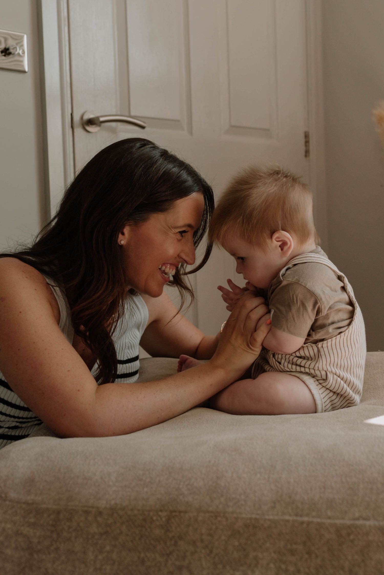 A tender moment between parent and child lying on a beige couch in a warm, natural light setting.