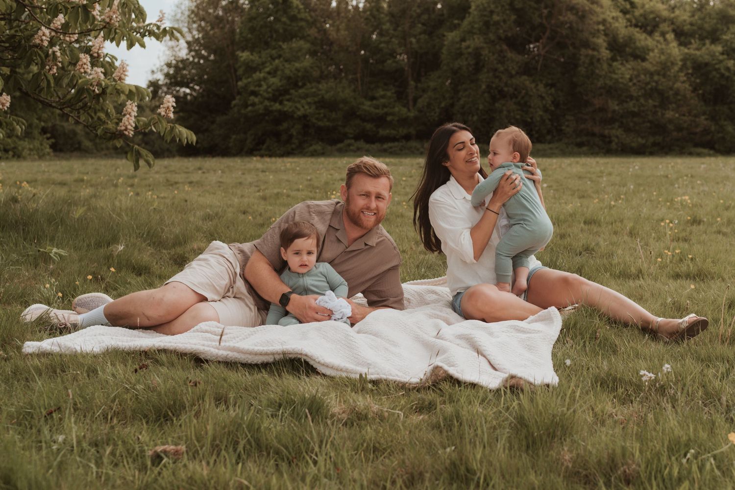 Family lying on blanket in grassy field during outdoor photo session.