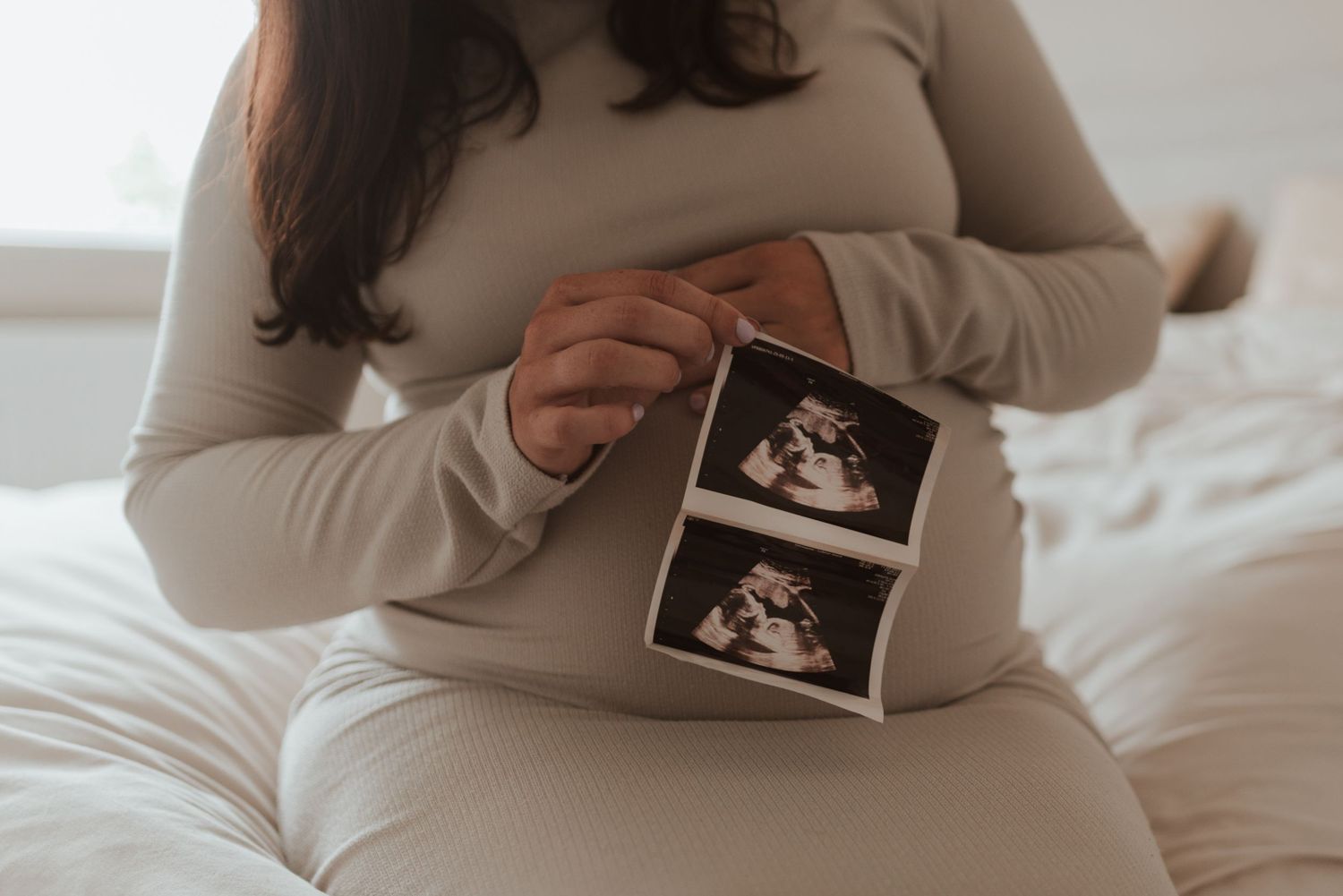 Sonogram ultrasound photo being held against white bedding in natural light.