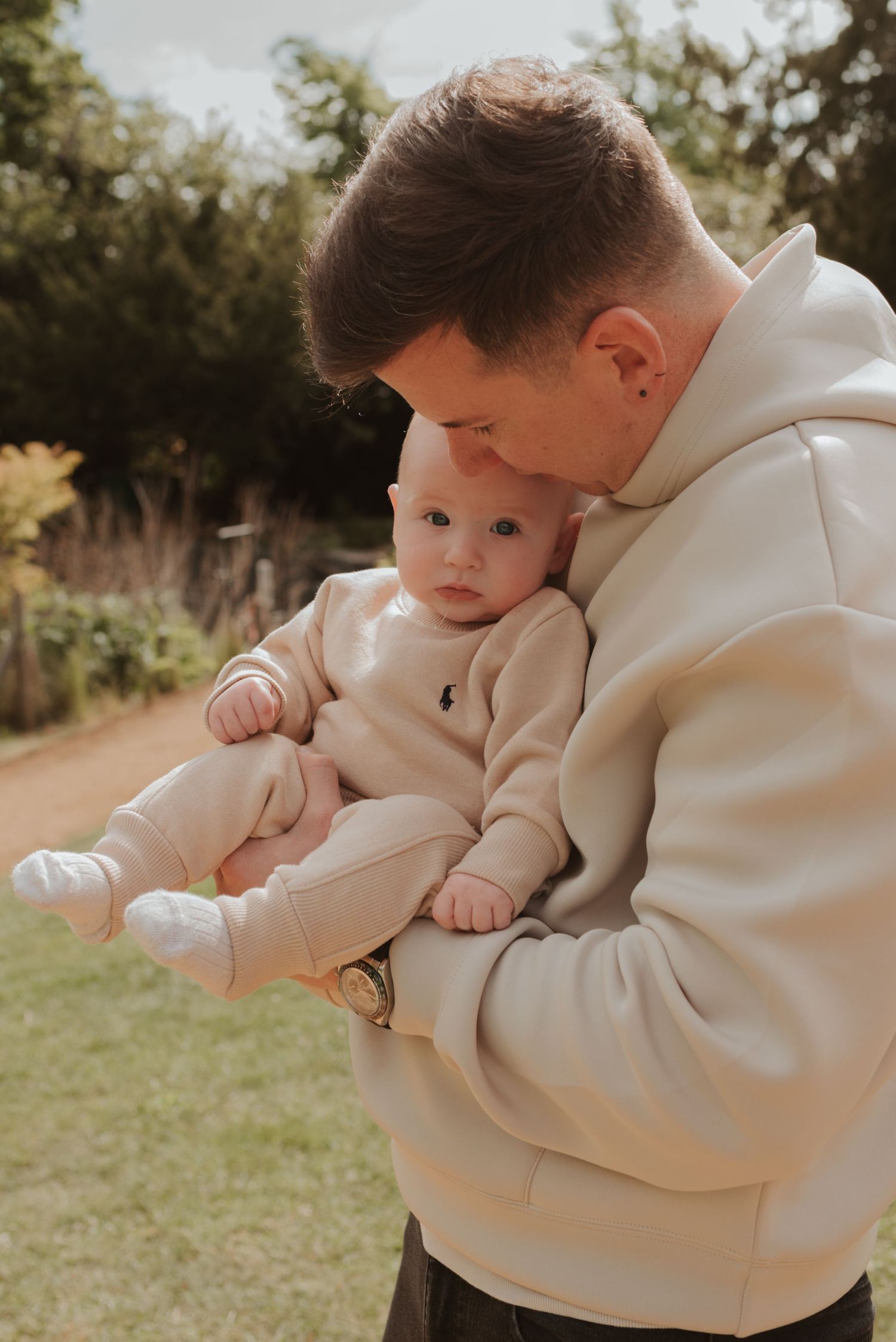 Tender moment between parent and baby both wearing matching cream colored outfits in garden setting.