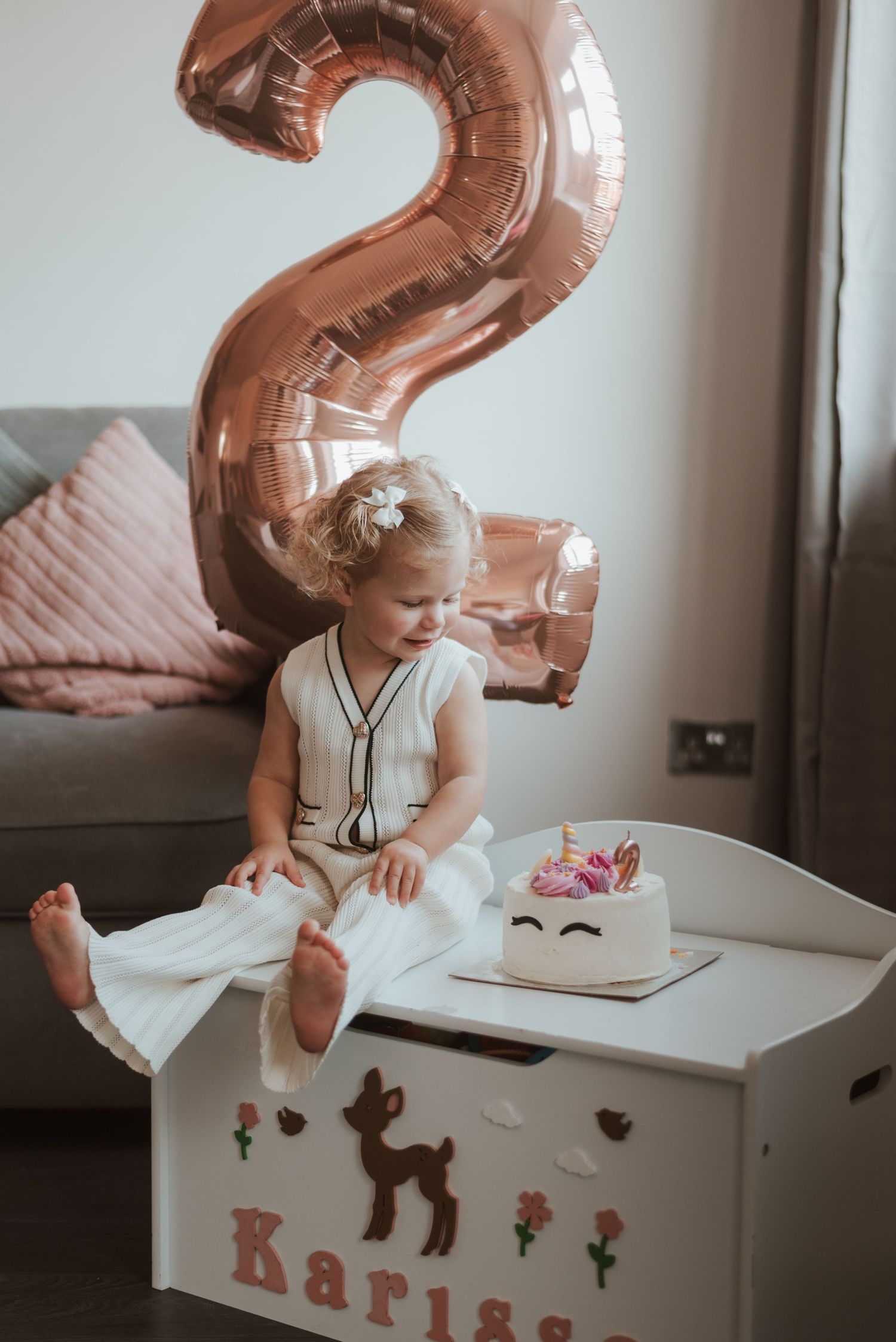 Gold number 2 balloon floats above a white toy chest in a cozy room.