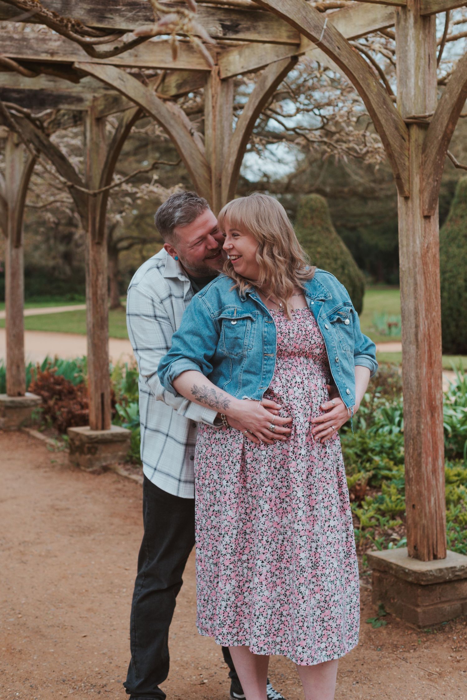A romantic maternity session under rustic wooden pergolas in a garden setting.