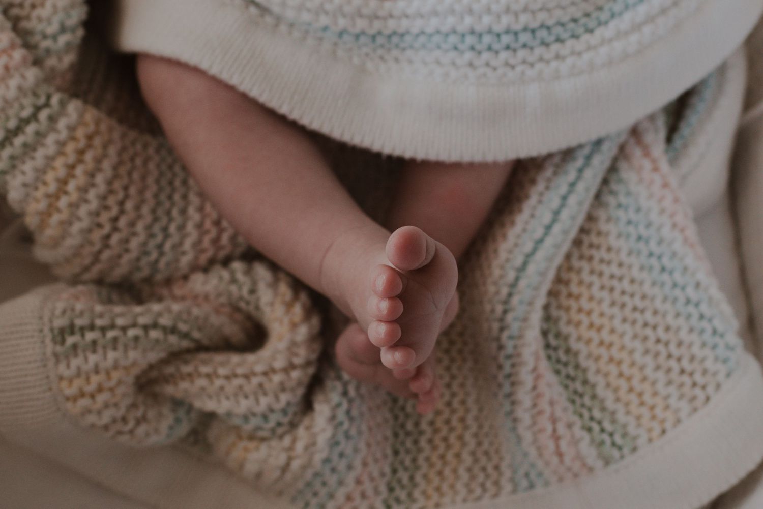 A tiny baby foot rests on a soft knitted blanket in cream and pastel blue tones.