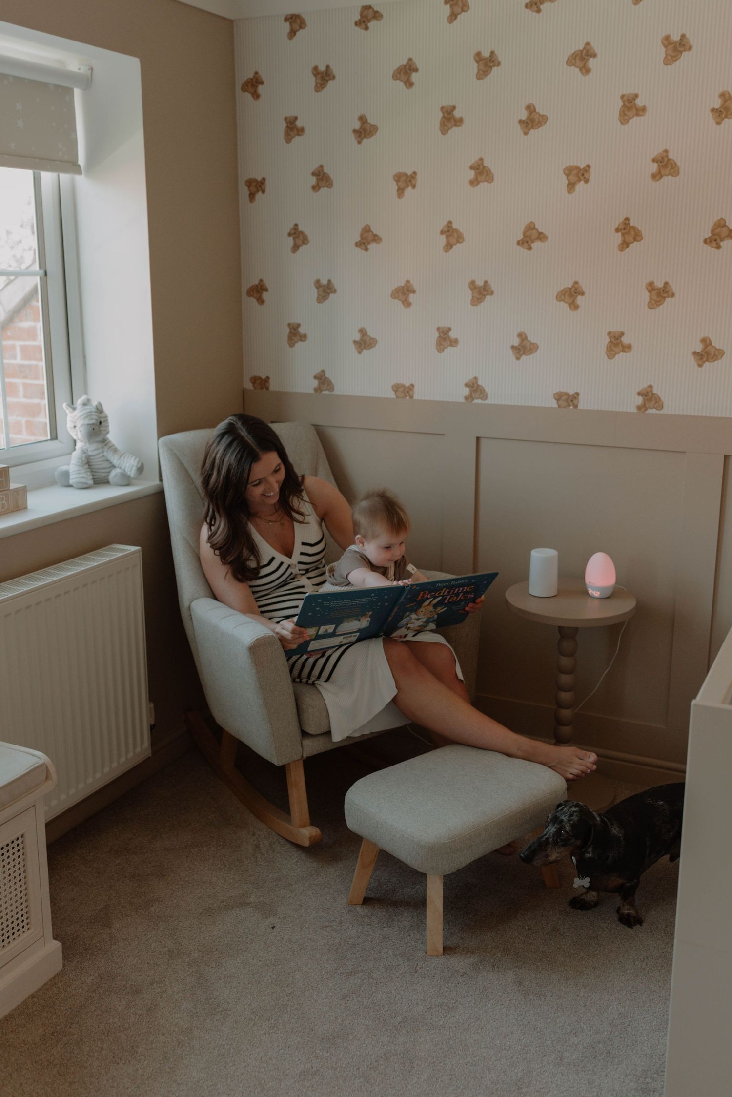Cozy nursery room with butterfly wallpaper features parent and child sharing tender moments in a comfortable grey armchair.