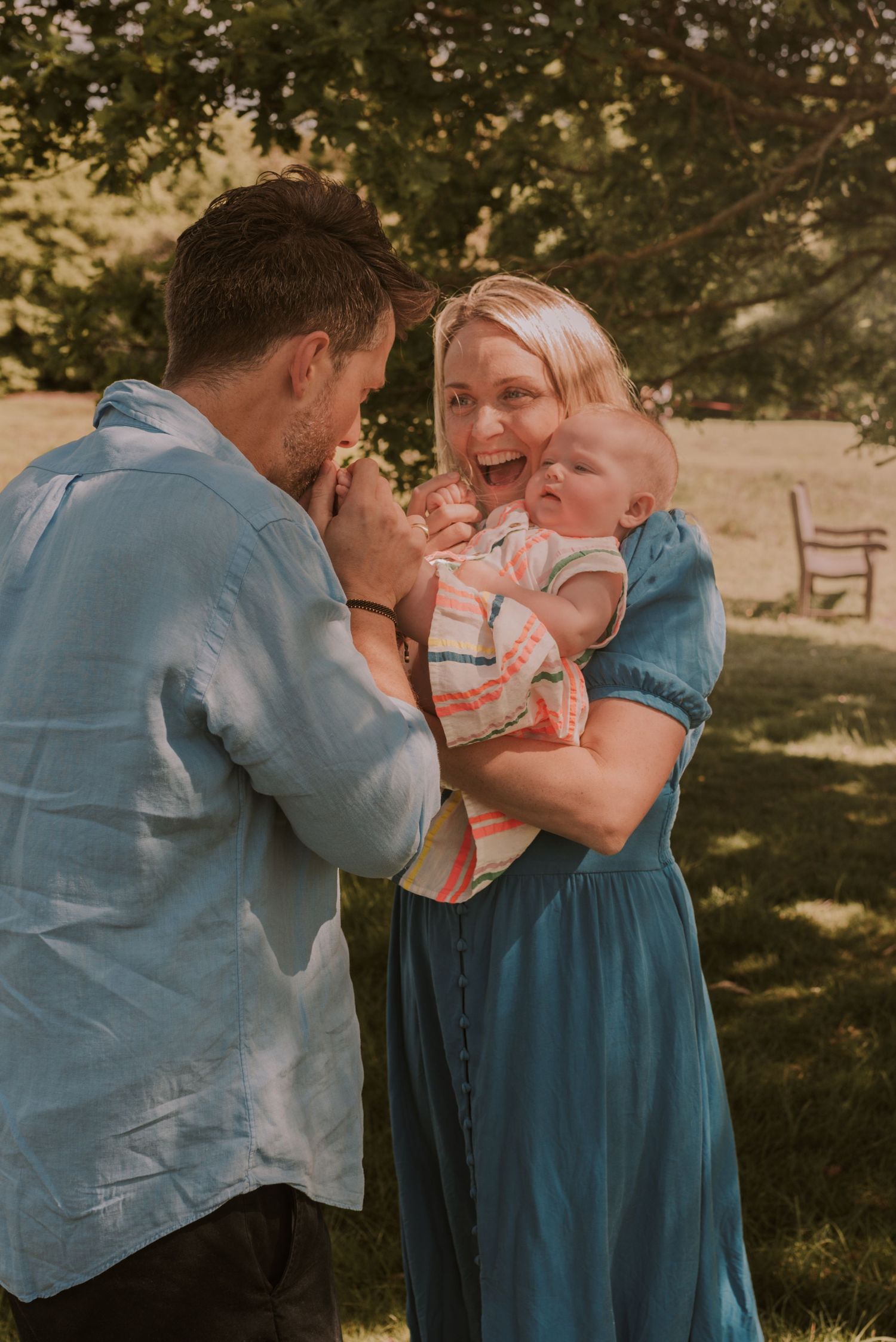 A joyful family moment outdoors with a baby being held in a blue dress and denim shirt setting.
