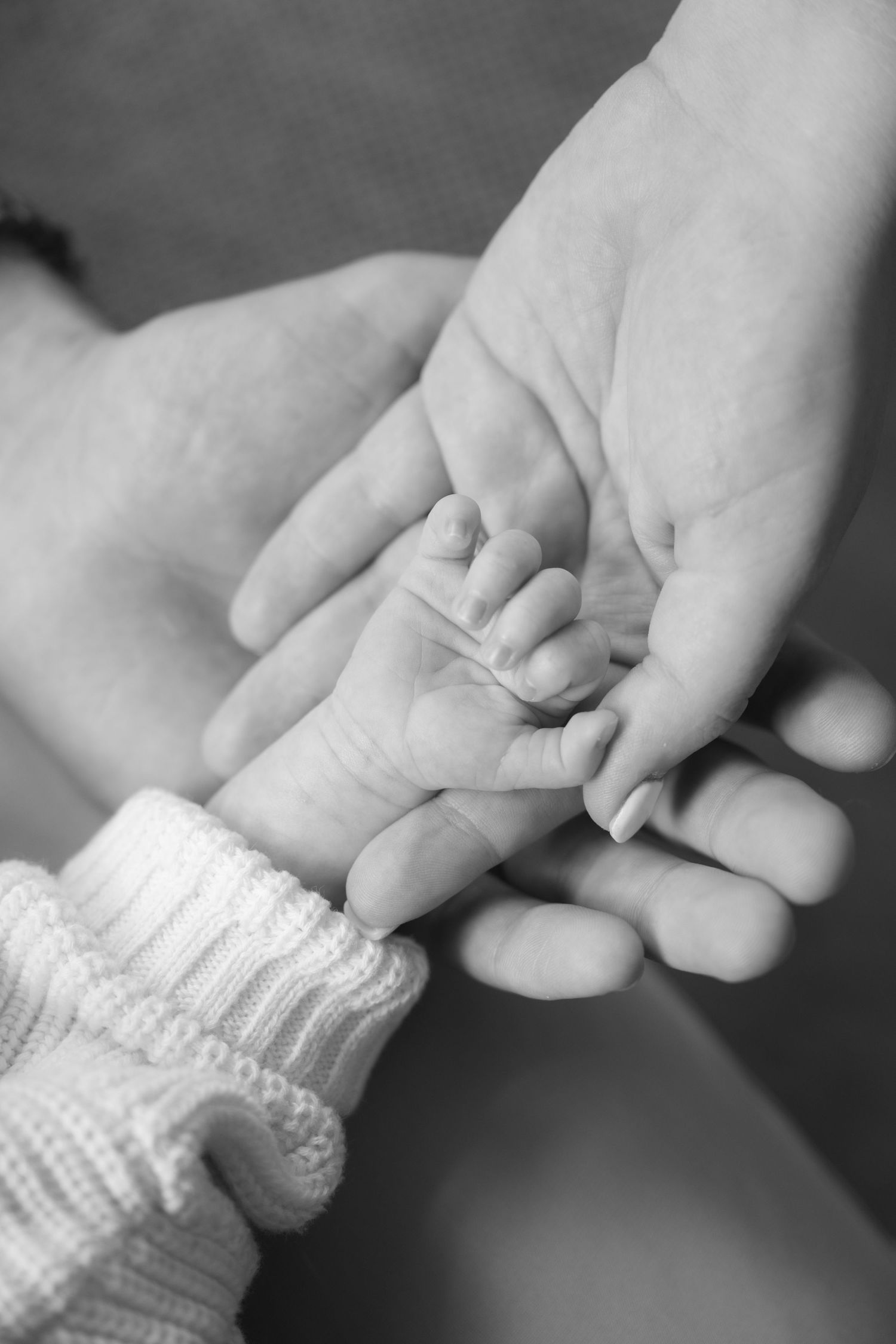 a newborn baby's hand is rested upon her mom and dad's hands during a lifestyle in home newborn session in Hudson, WI.