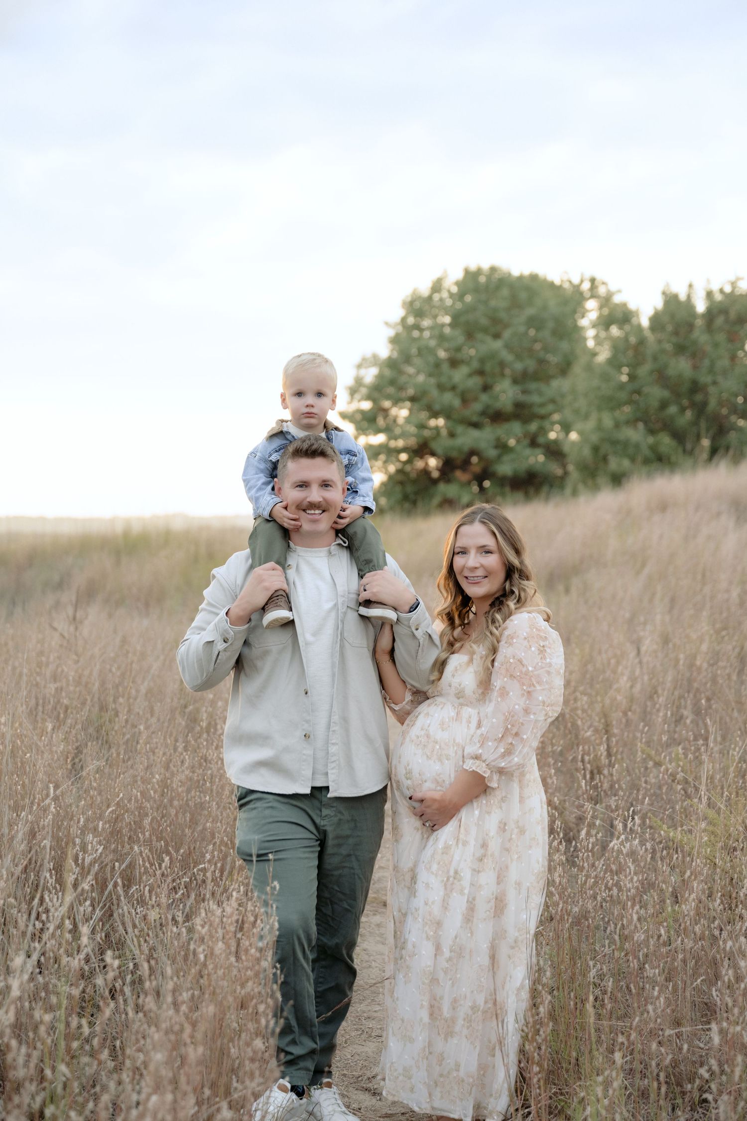 Young parents hold pregnant belly and toddler during outdoor family photos in cottage grove, MN.