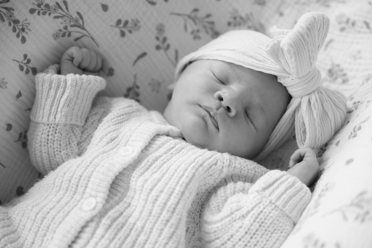 Sleeping newborn with a knit sweater and big bow on her head in studio family session in Stillwater, Minnesota.