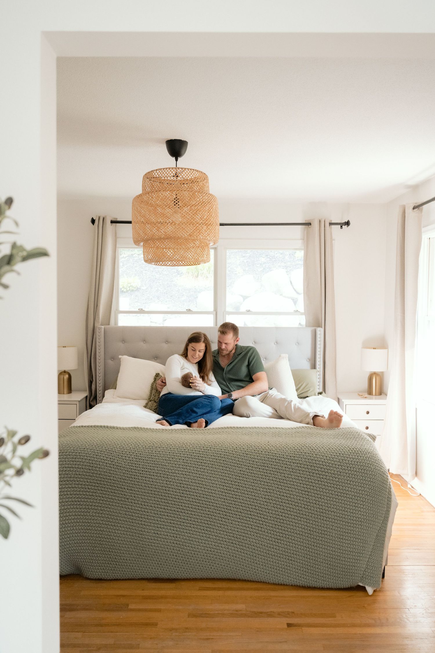 a couple snuggles their newborn on the bed in a brightly lit bedroom during a lifestyle in home newborn in the Twin Cities, MN.