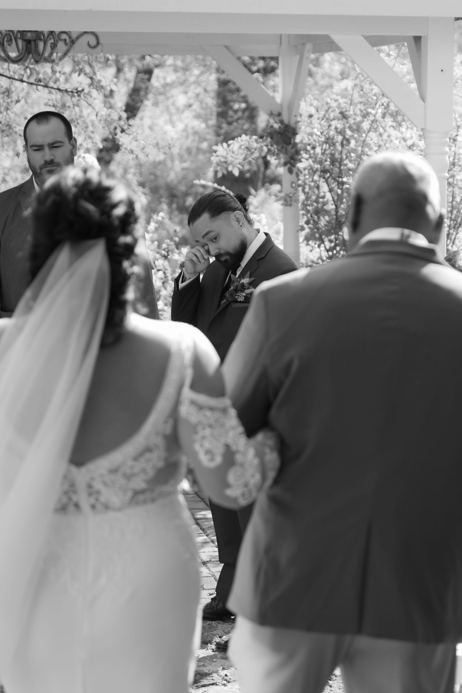 Groom wipes a tear from his eye as his bride walks down the aisle during an outdoor wedding at Trellis in Stillwater, MN.