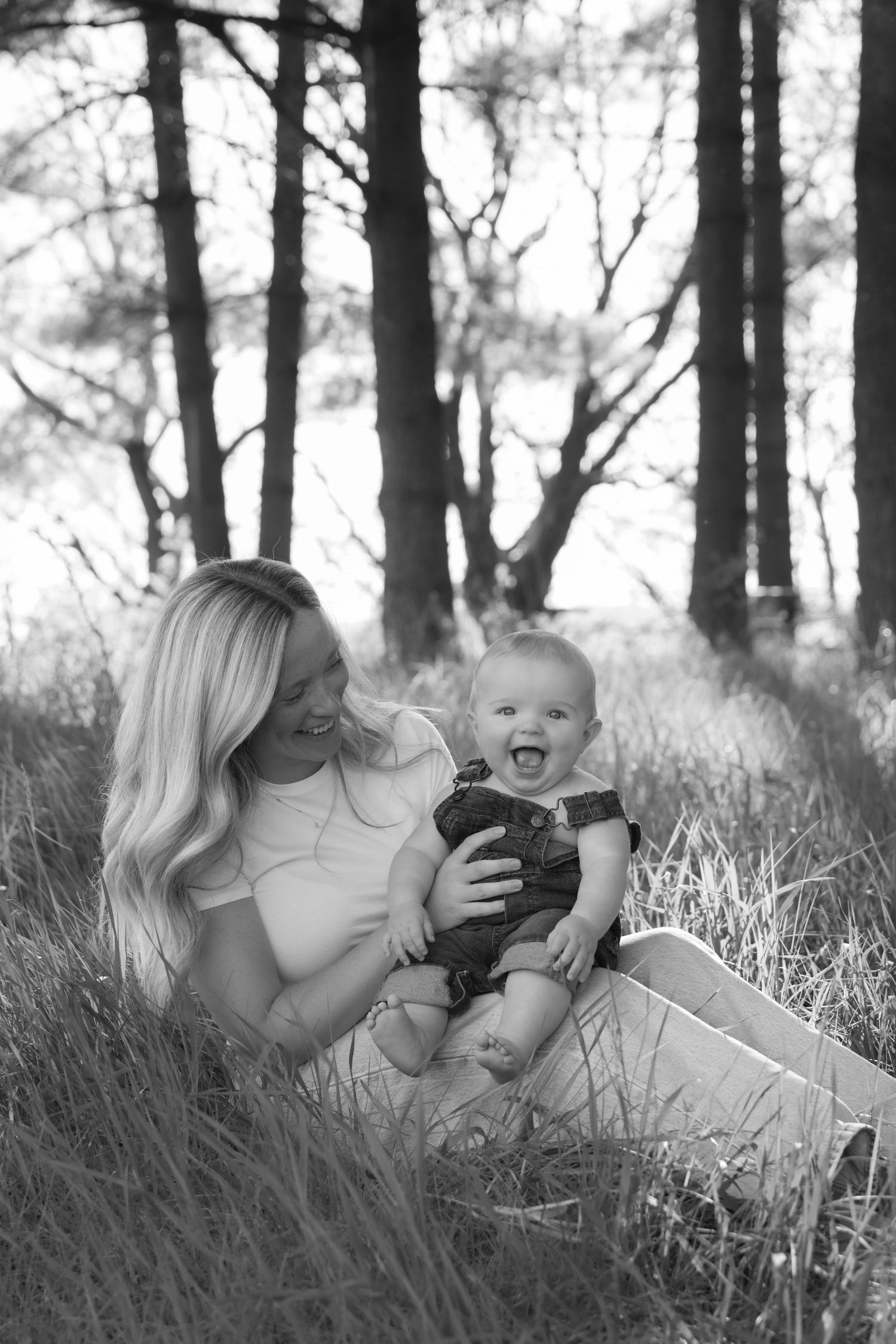 Mom holds her baby in a grassy field as he smiles at the camera during an outdoor lifestyle family session in Hudson, WI