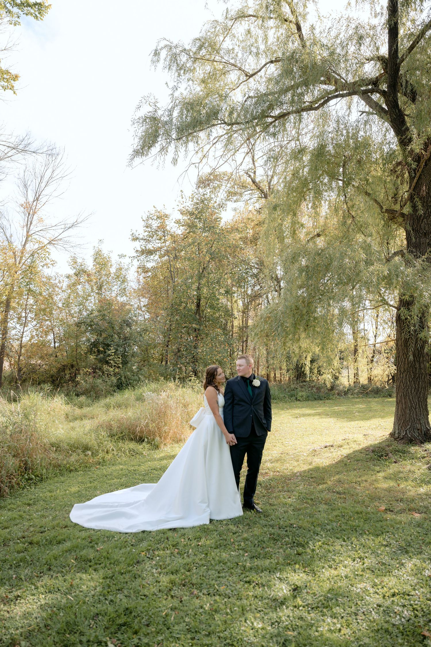 bride and groom looking at each other on their wedding day, a willow tree in the background at abella farms in chisago city mn