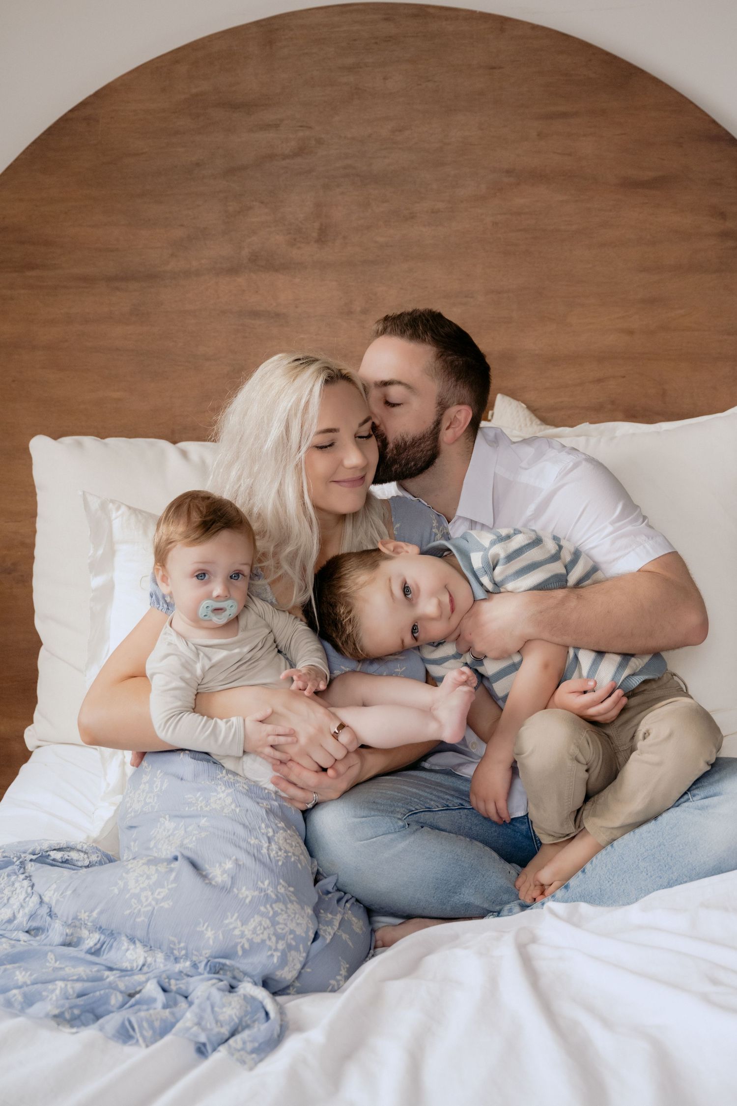 Family with two young kids cuddled on a bed smiling during an in studio session in Stillwater, Minnesota.