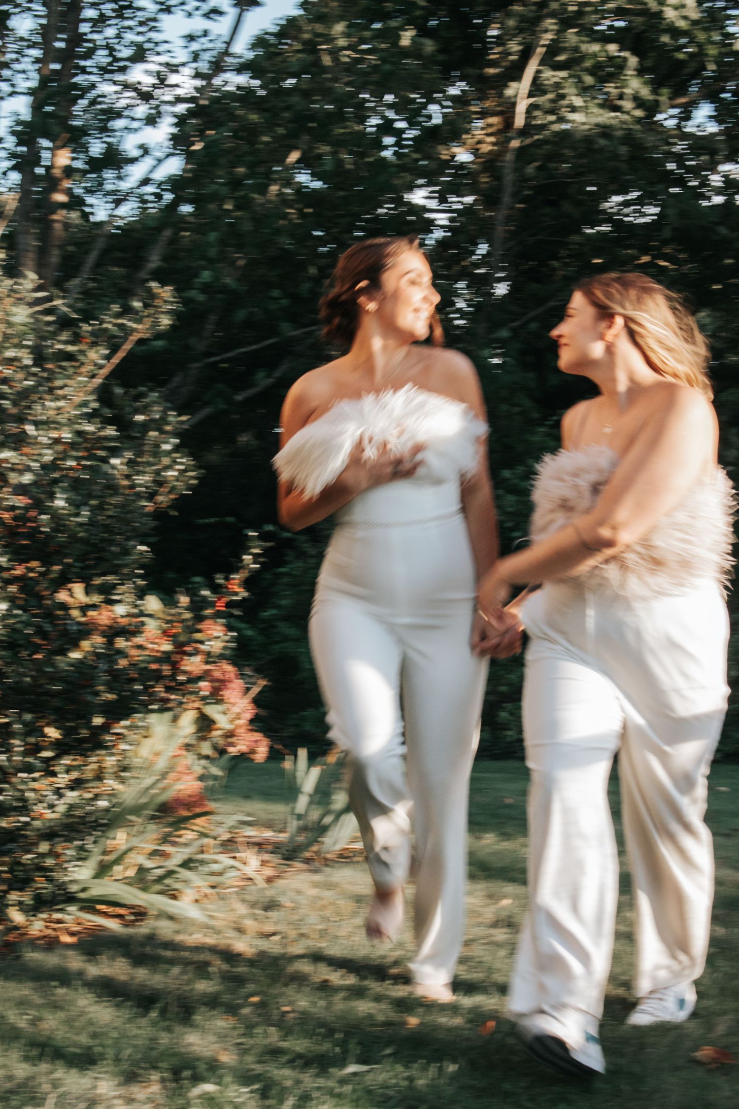Two people in white outfits share a joyful moment in a garden setting.