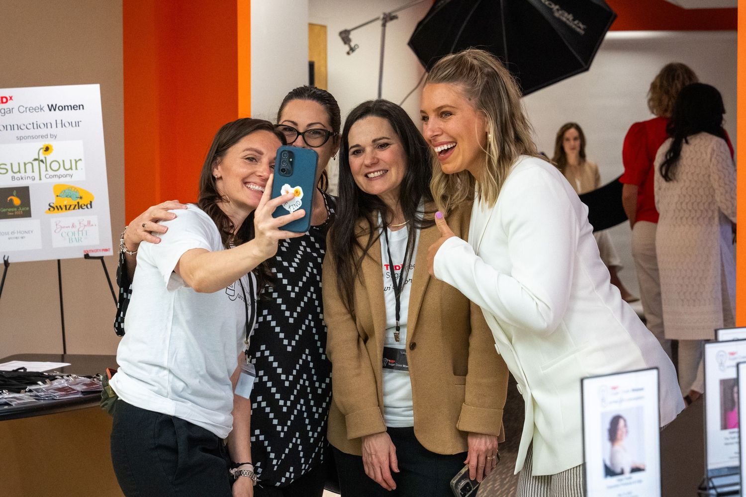 Four women taking a selfie together at an indoor networking or promotional event.