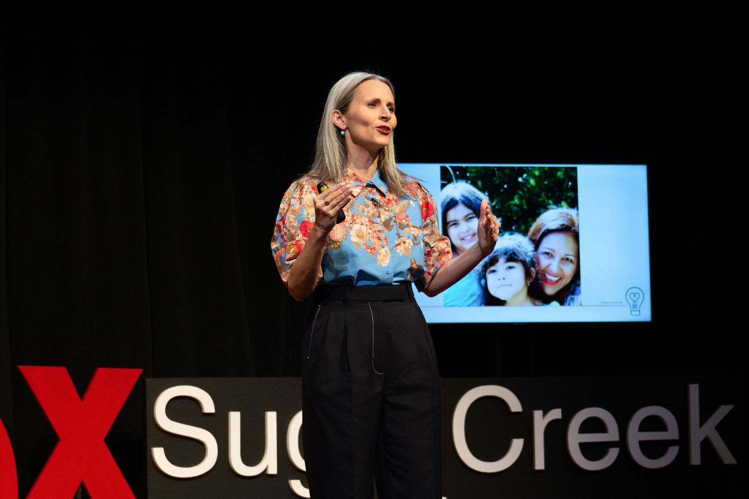 Woman presenting on TEDxSugar Creek stage holding a family photo during her talk.
