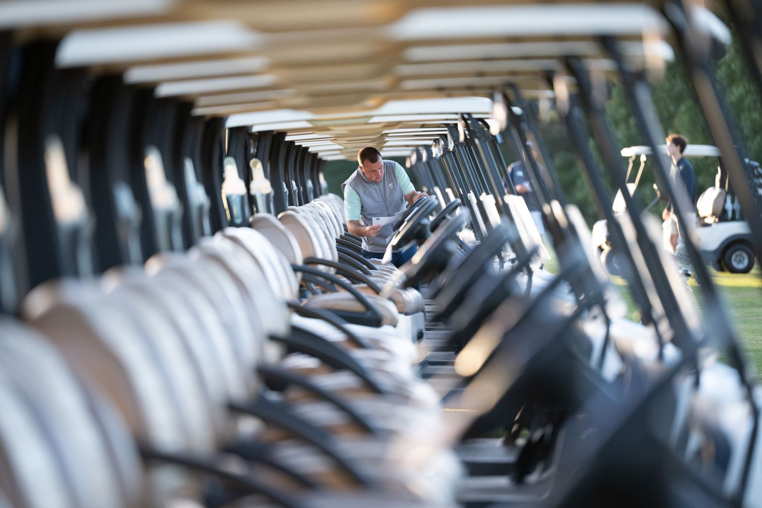 Row of white golf carts lined up in cart barn with person walking between them.