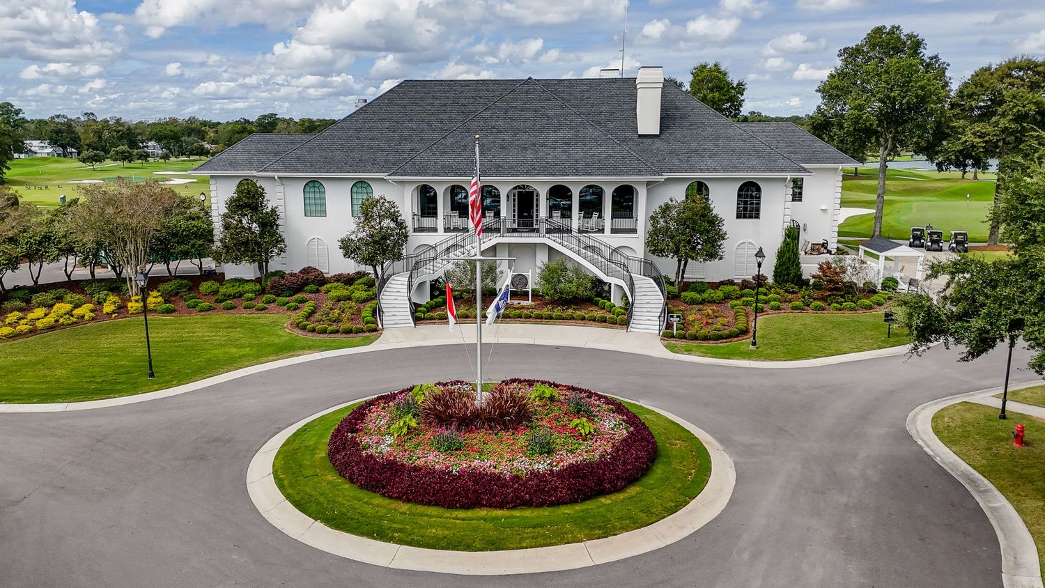 Aerial view of elegant white golf club clubhouse with circular flower garden entrance.
