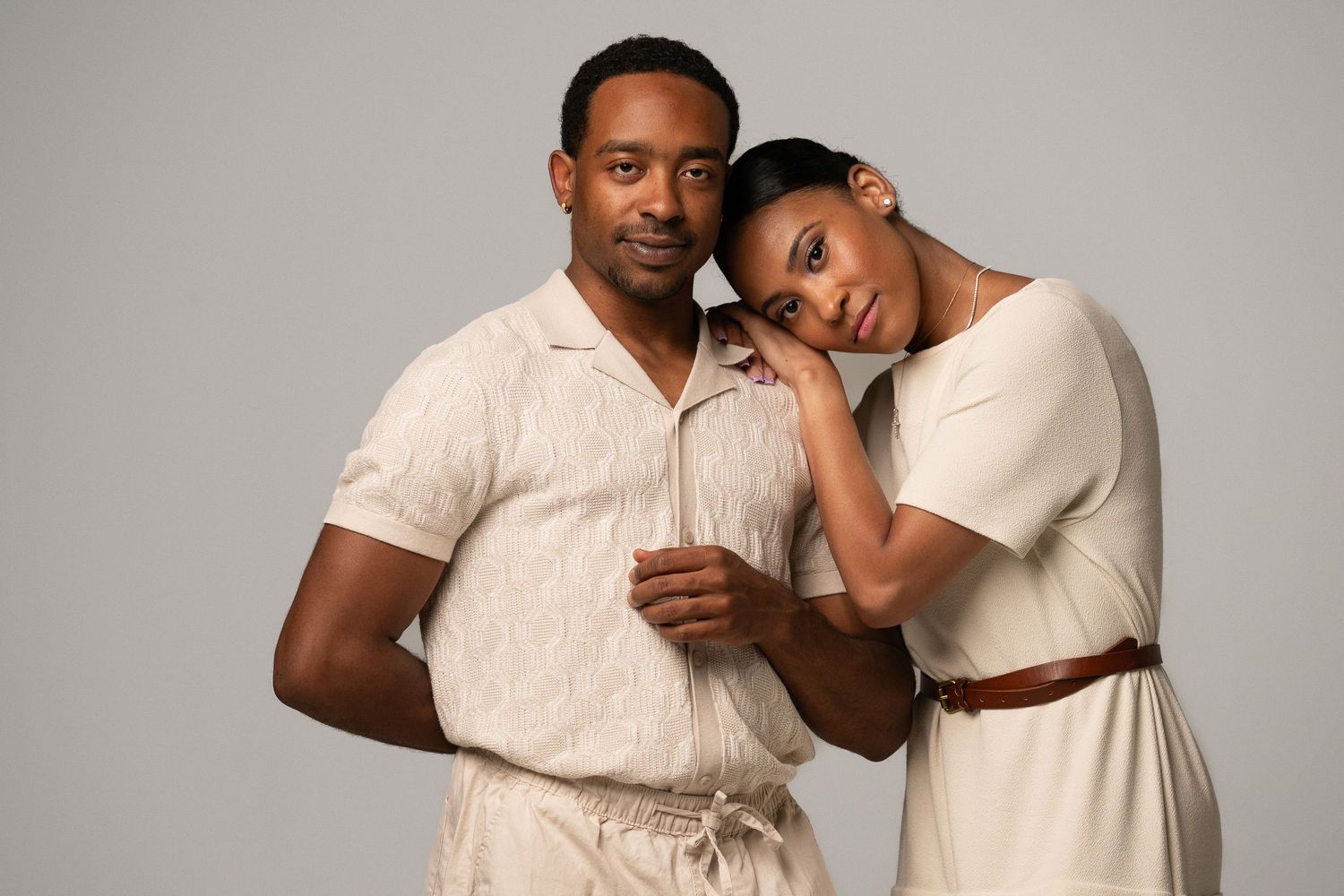 Couple in matching cream outfits posing together against gray background in studio portrait.
