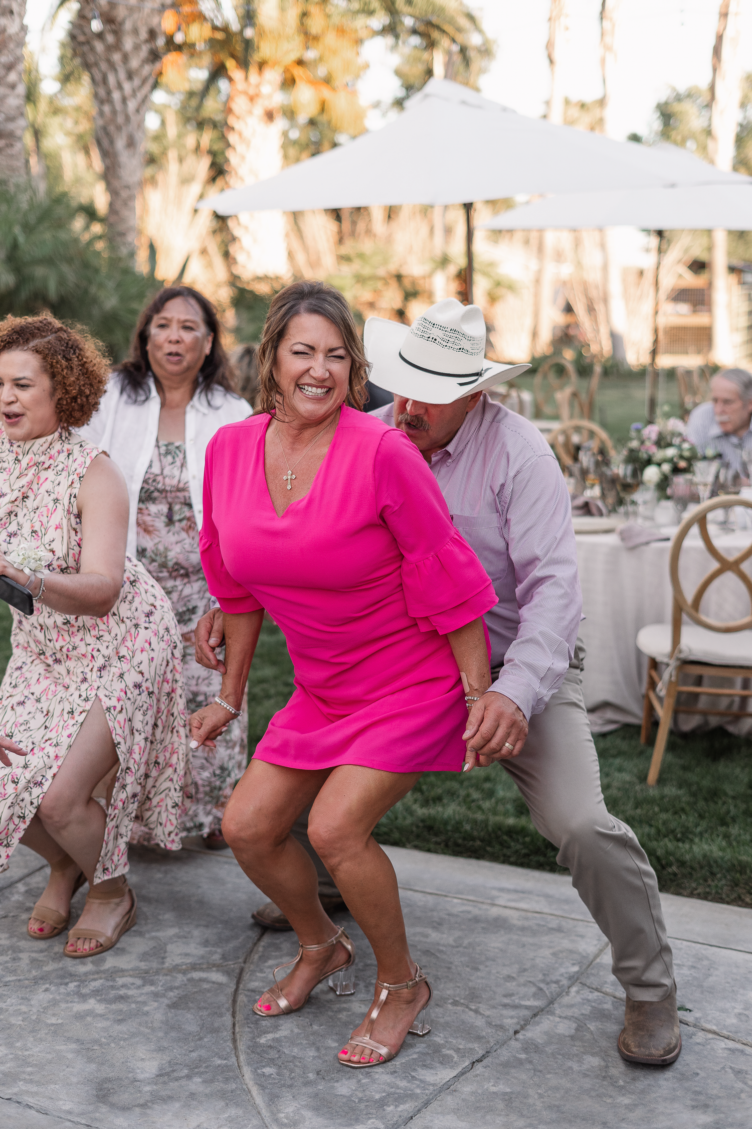 Wedding guests dancing and having fun at an outdoor reception under palm trees.