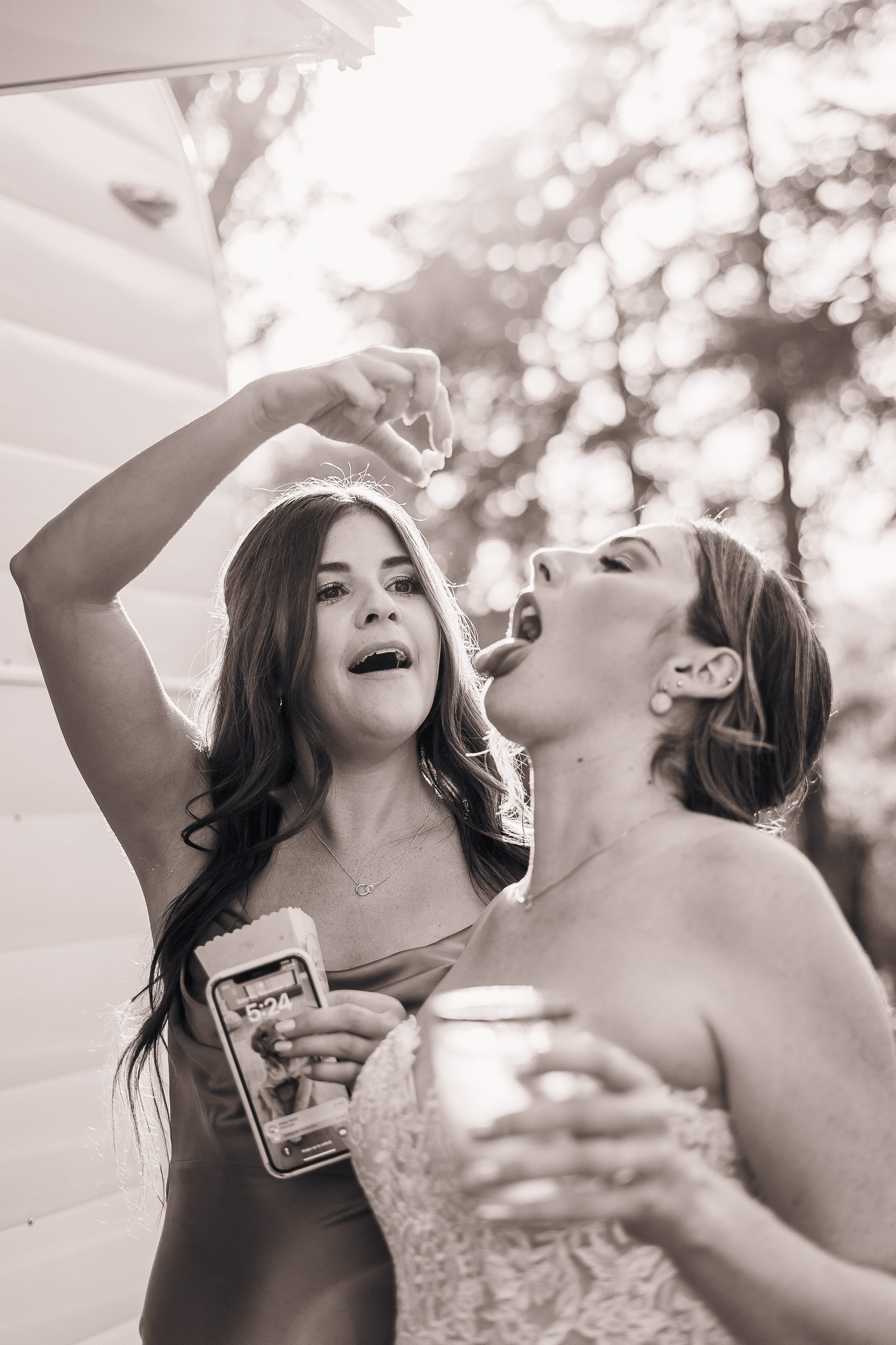 Candid moment of bride and bridesmaid shots outdoors in black and white photography.