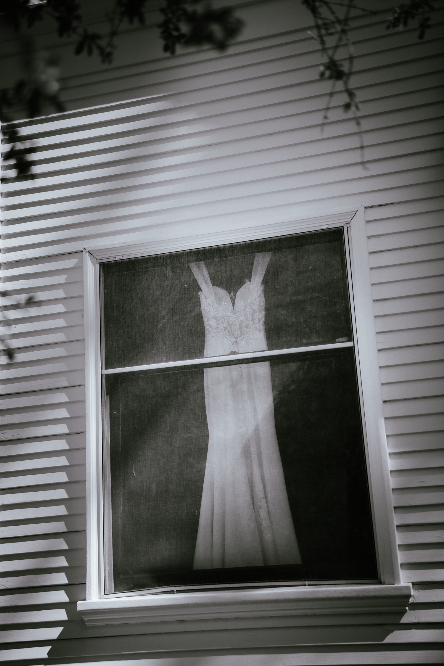 White wedding dress displayed in window of classic white siding house.