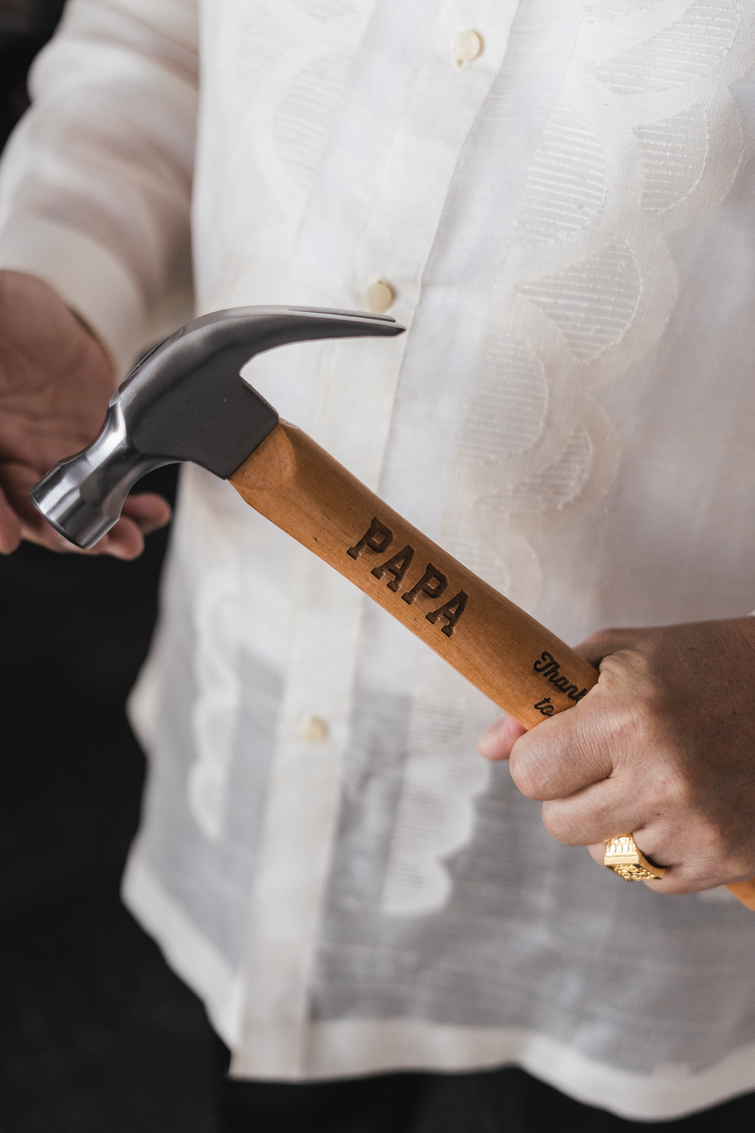 Bride's dad holding a hammer labeled 'Papa' at a wedding celebration.