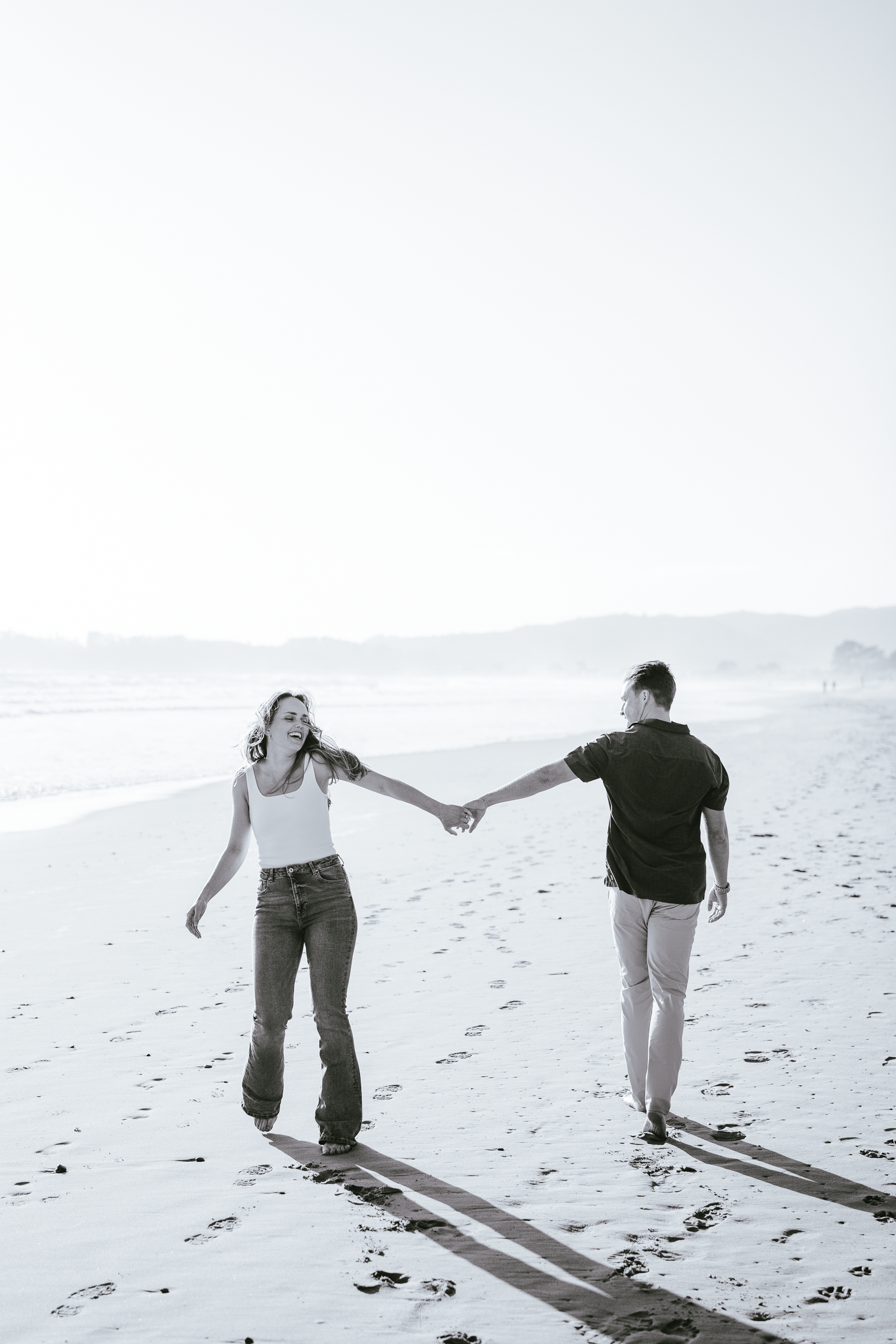 Black and white photos of couple walking and holding hands on beach leaving footprints in sand at Stinson Beach in Marin County.