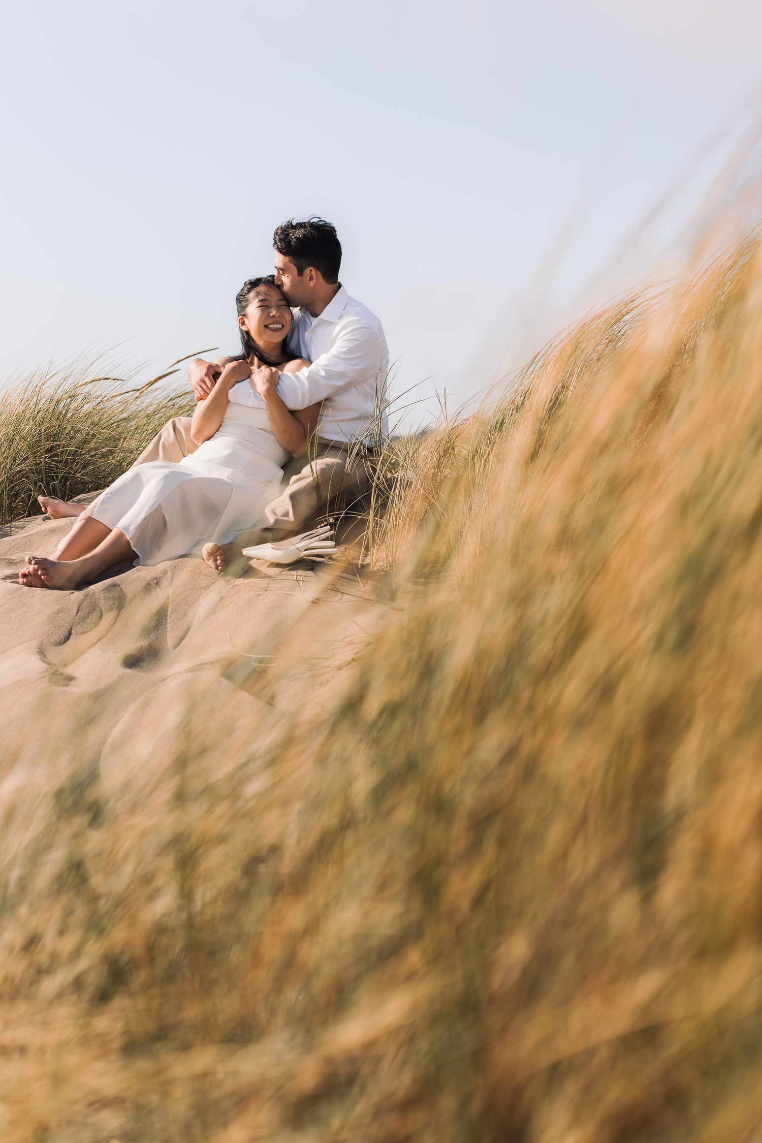 Couple rests among tall beach grass during golden hour photoshoot at Ocean Beach in San Francisco.