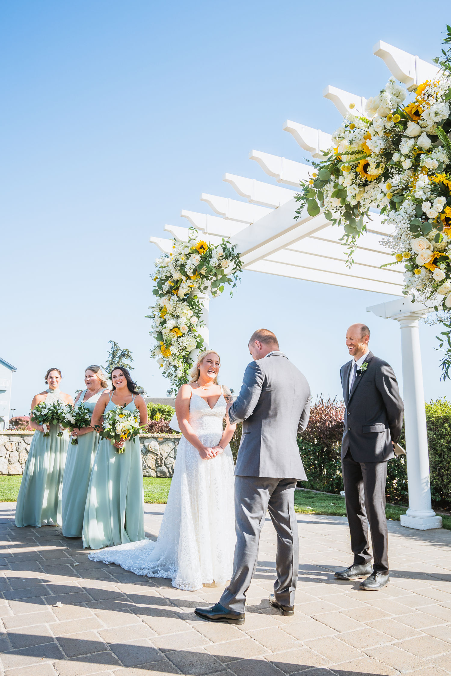 Outdoor wedding ceremony under a white pergola decorated with yellow and white floral arrangements at Oceana Hotel and Spa in Half Moon Bay.