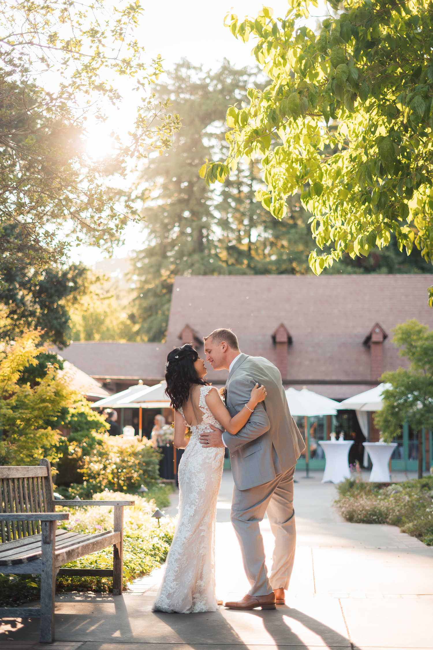 A romantic outdoor wedding moment with a couple sharing a kiss on a garden path during golden hour sunlight.
