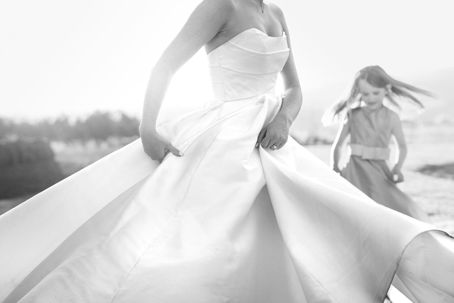 Black and white photo of flowing white dress fabric swirling in motion outdoors.