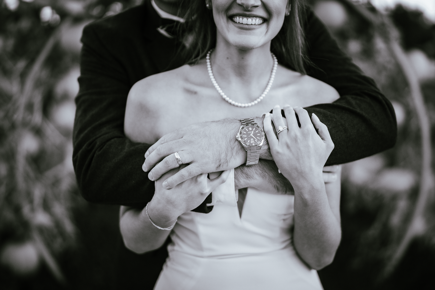 Black and white close-up of couple embracing showing wedding ring and pearl necklace at Cornerstone Sonoma.