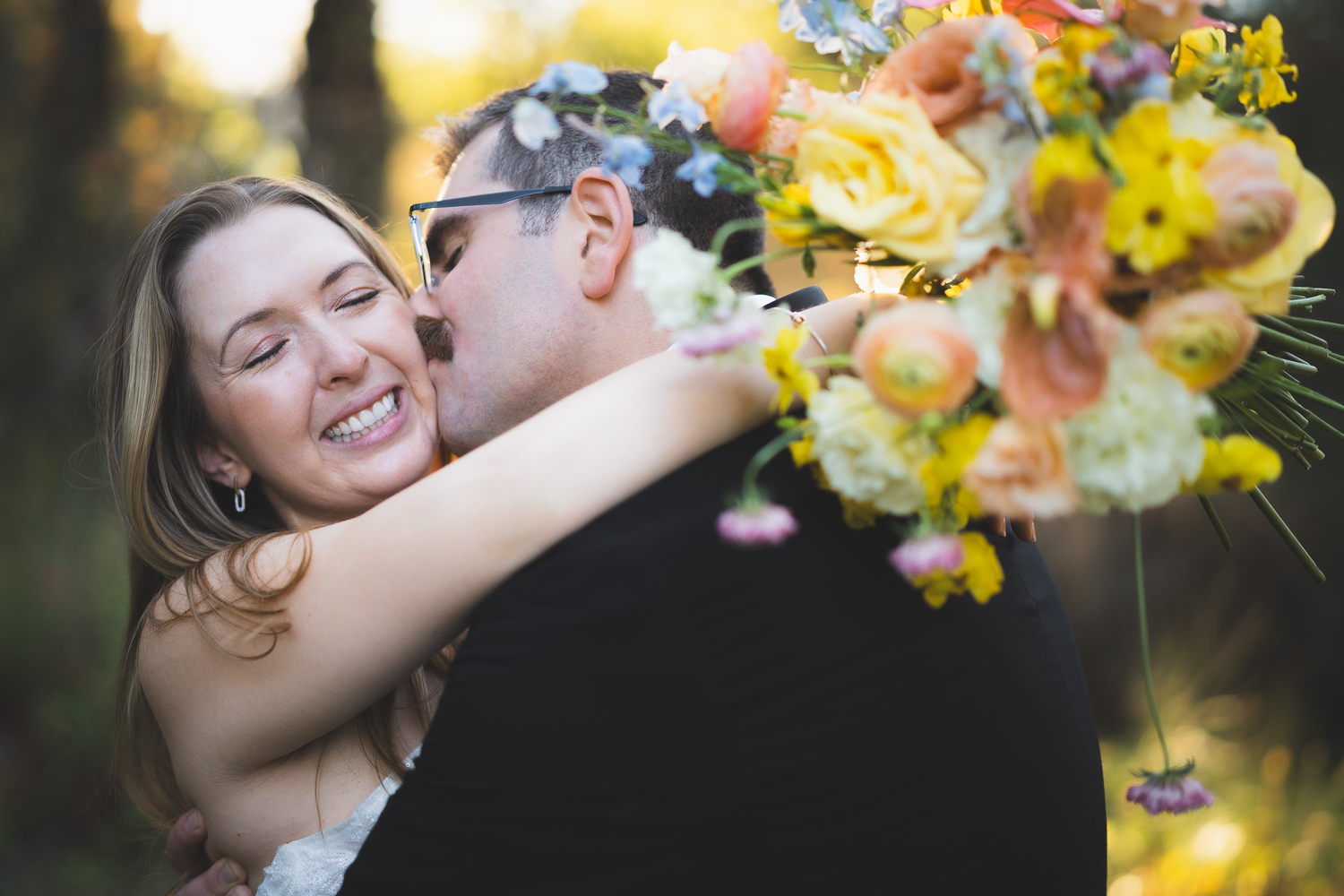 Romantic wedding couple embraces with yellow flowers in soft focus at Yokayo Ranch in Ukiah.