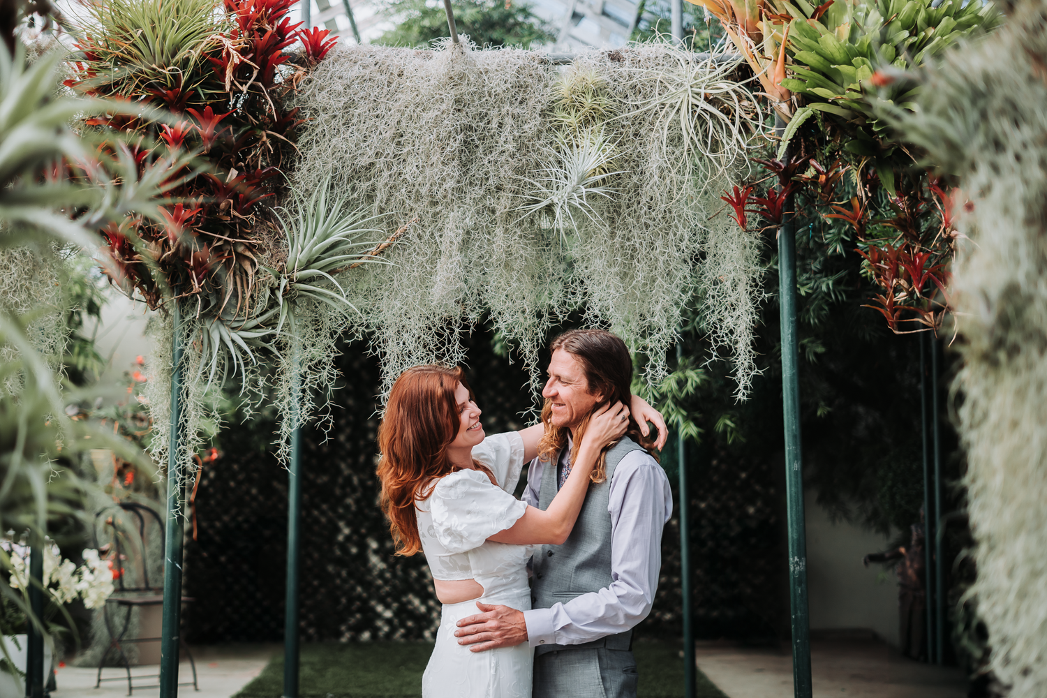 Romantic engagement photoshoot in greenhouse garden setting with lush greenery and red floral accents at Shelldance Orchid Farm in Pacifica.