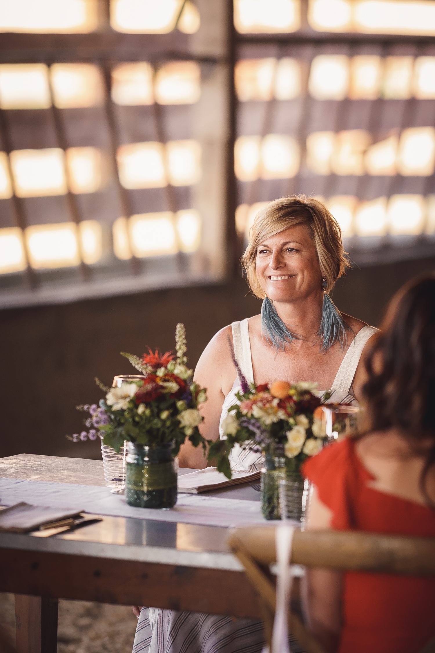 Wedding reception table settings with floral centerpieces and natural lighting through windows and a smiling guest at Cow-Track Ranch.