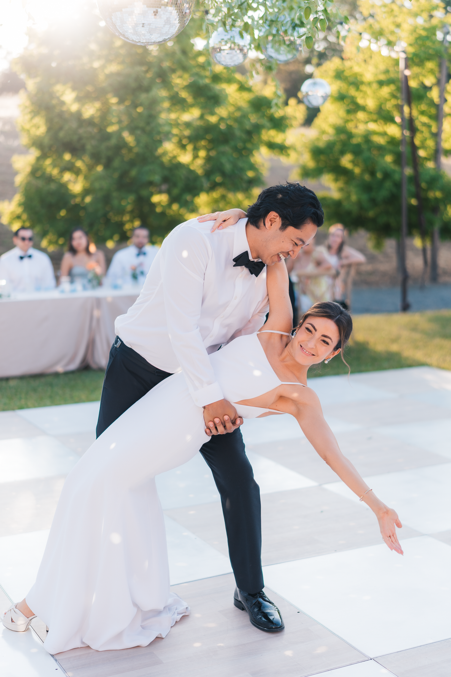 Couple performs romantic dip dance move on white dance floor during wedding reception.