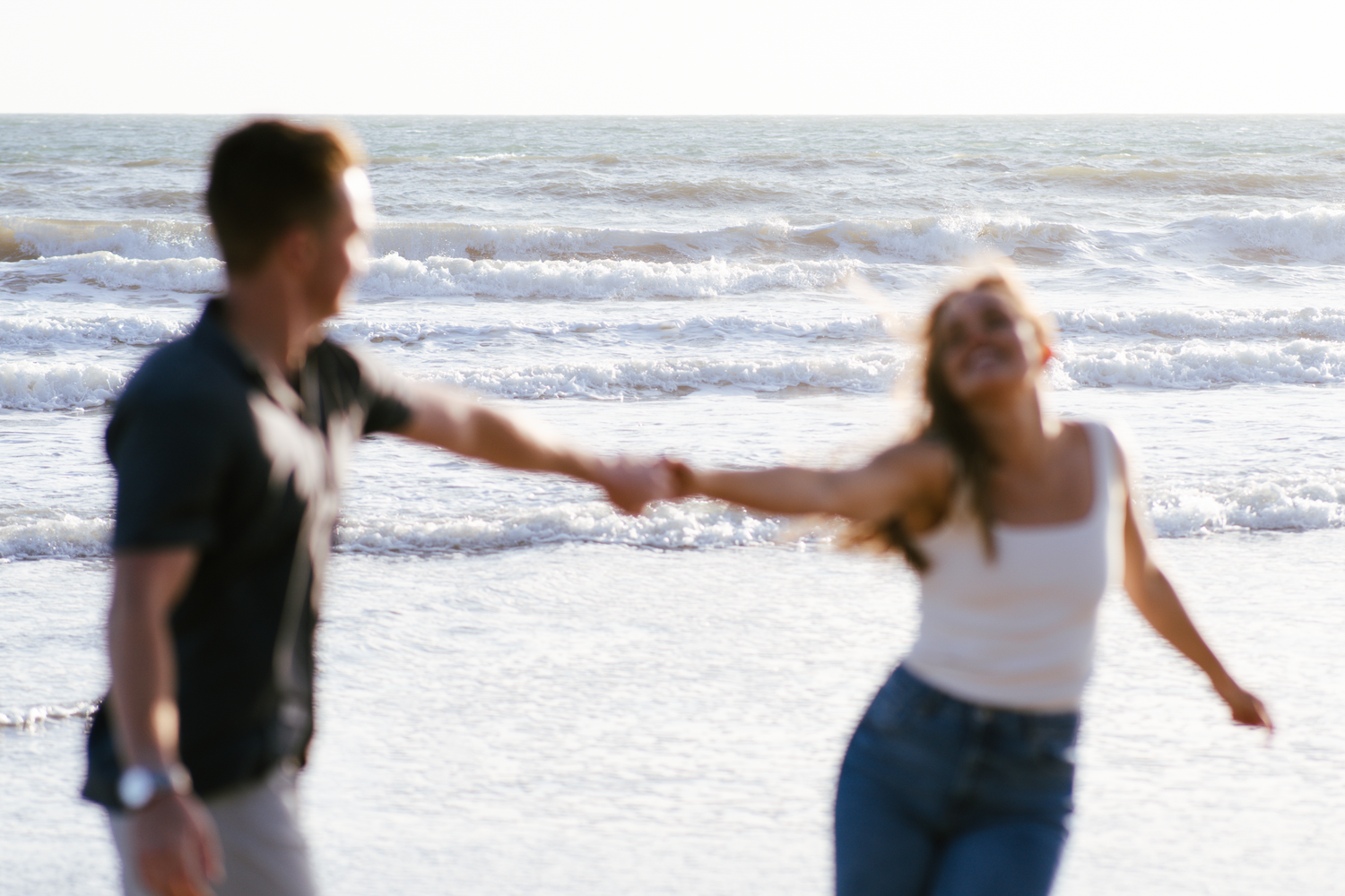 Couple holding hands while walking along a beach shoreline during engagement photoshoot at Stinson Beach in Marin County.