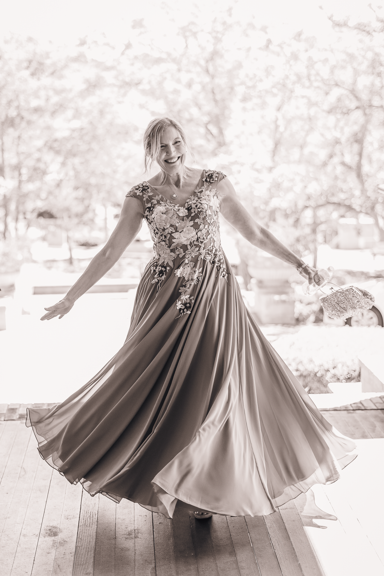 Mother of bride twirls in flowing dress showing movement in black and white photos.